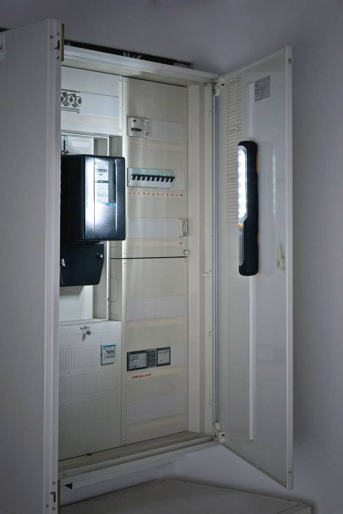 Un boîtier de fusibles ouvert avec des interrupteurs et des câbles visibles sur un mur. Des installations électriques sont apparentes.