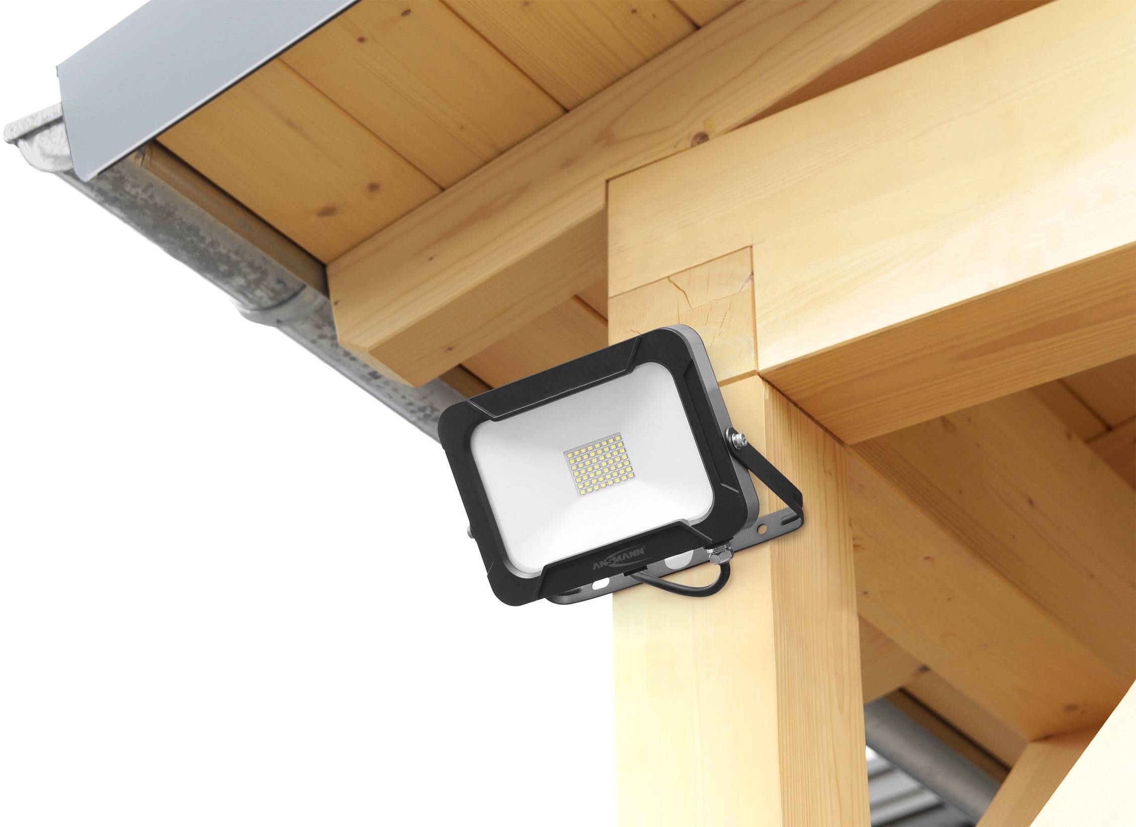 Un projecteur LED est fixé à une poutre en bois sous un toit, éclairant vers le bas et protégé des intempéries.
