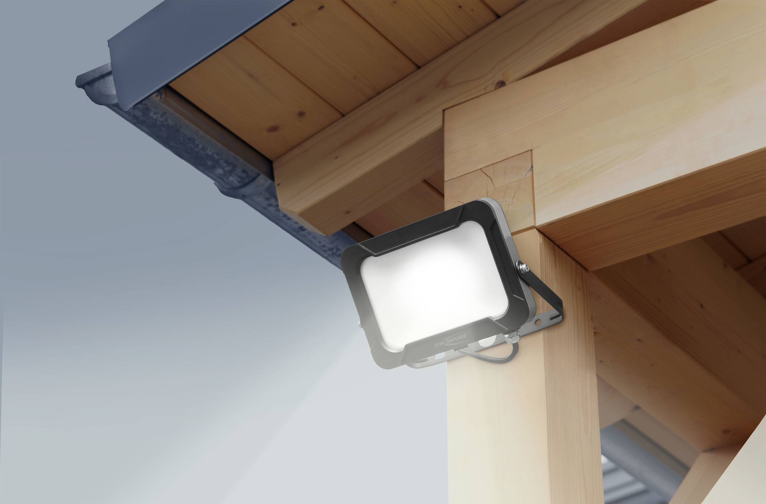 Un projecteur noir est fixé à un poteau en bois d'un bâtiment moderne et éclaire vers le bas.