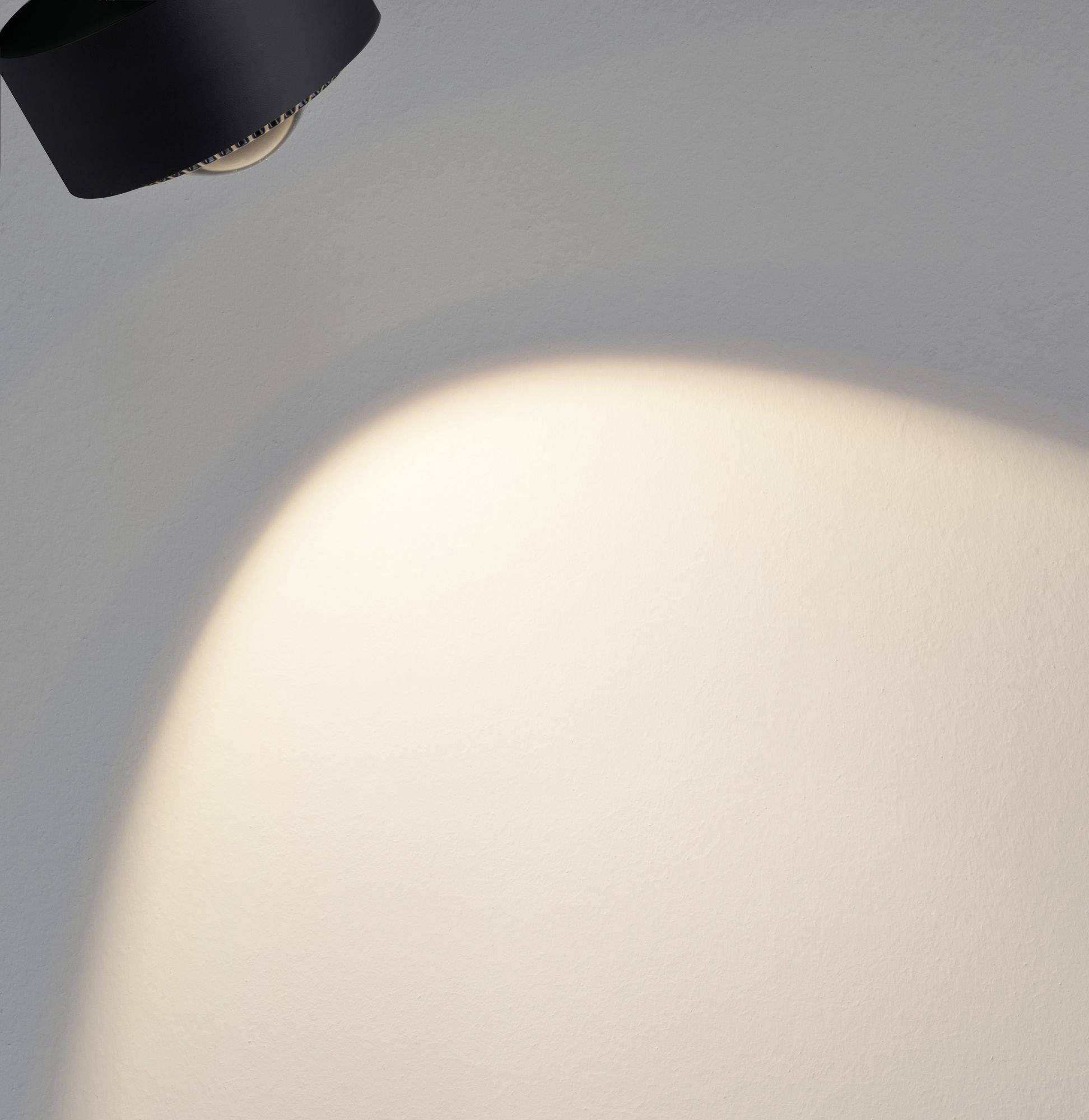 Un projecteur noir éclaire un mur gris et crée un cercle lumineux sur la surface.