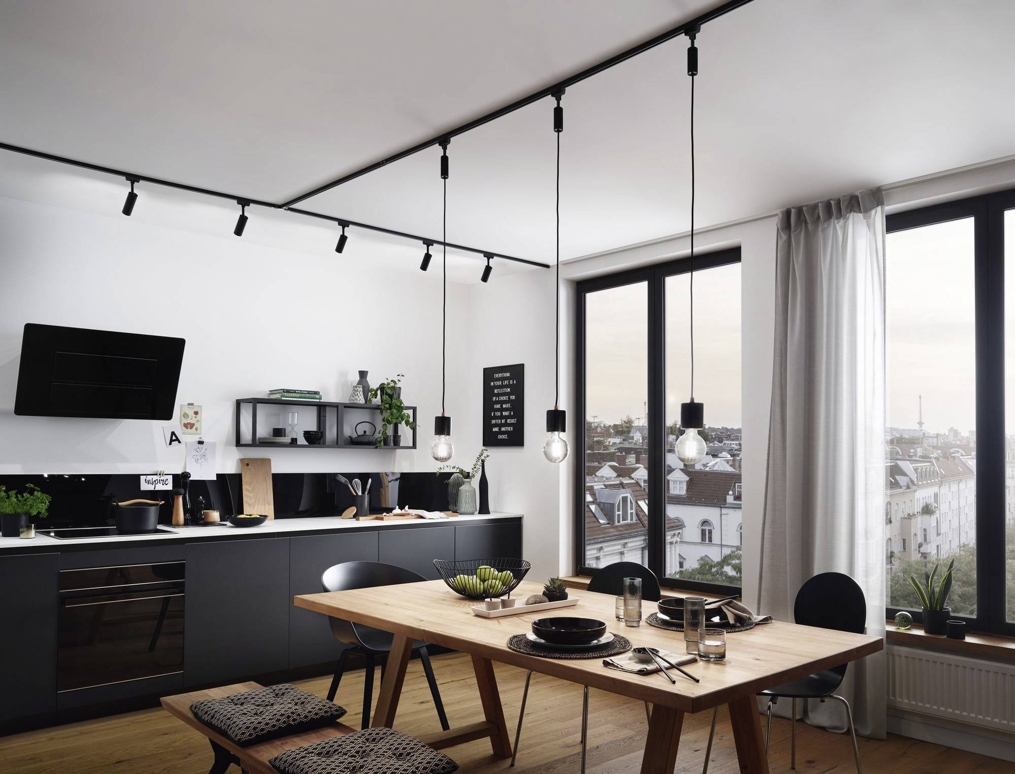 Une cuisine moderne avec espace repas. Armoires foncées, table en bois avec couvert pour deux personnes. Grandes fenêtres avec vue sur la ville.