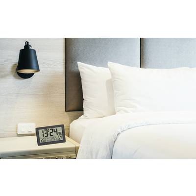 Horloge numérique affichant 13:24 sur la table de nuit à côté du lit avec des oreillers blancs et une couverture ; lampe moderne fixée au mur.