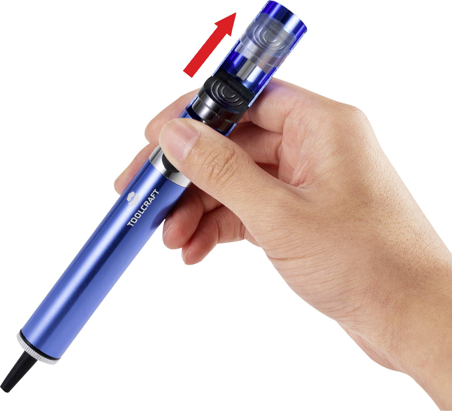 Une main tient une pompe de dessoudage bleue avec un marquage de flèche rouge indiquant le mécanisme de commande sur le dessus de la pompe.