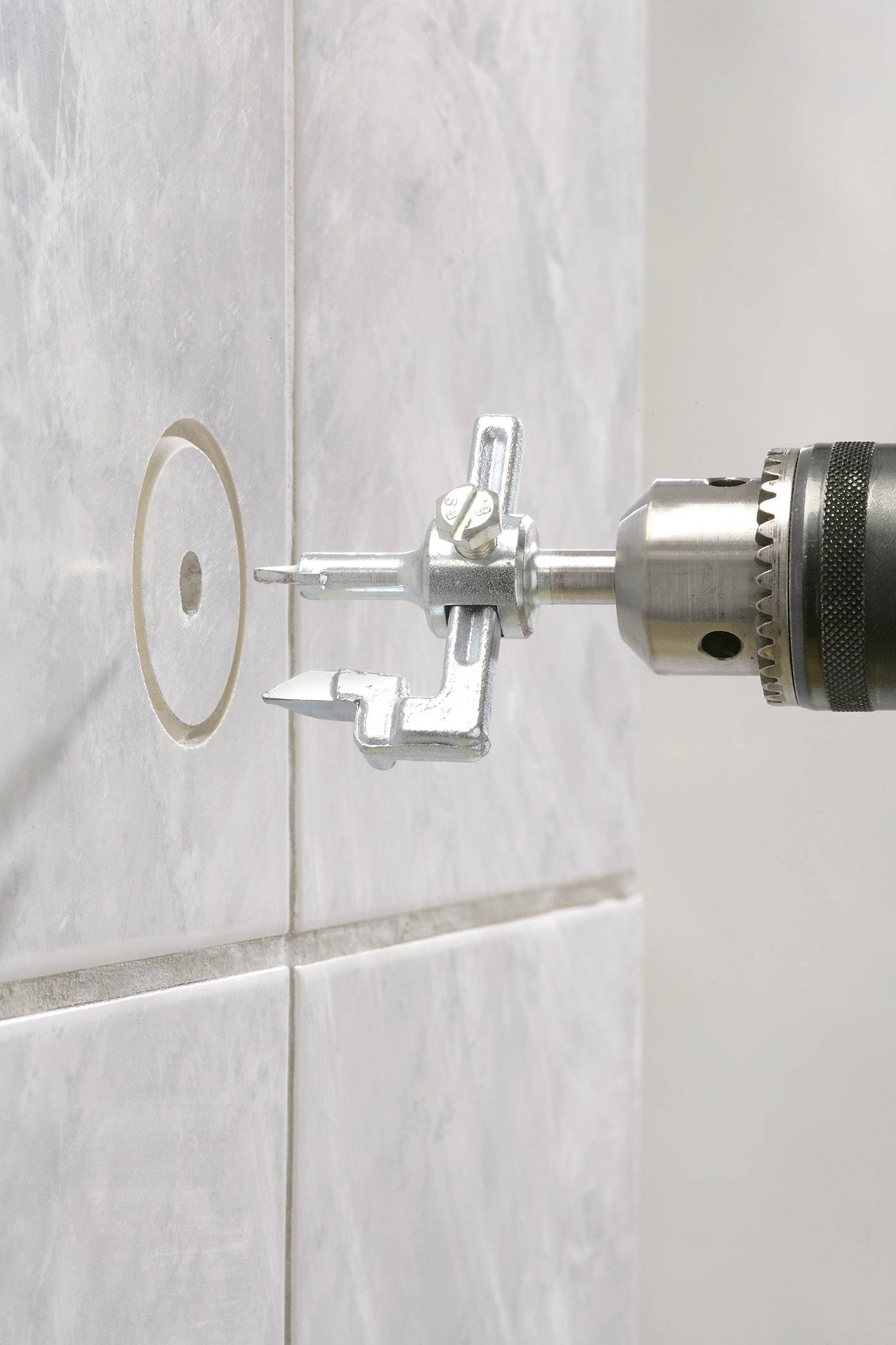 Une perceuse avec une scie-cloche découpe un trou rond dans un carreau de faïence sur un mur.
