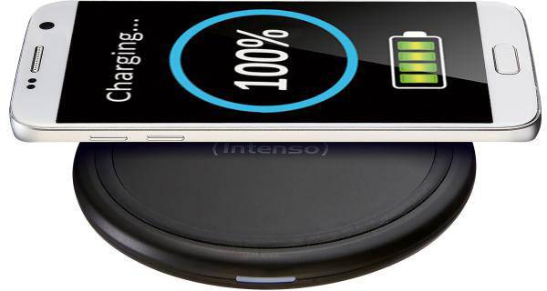 Un smartphone est posé sur un chargeur sans fil, son écran affichant 'Charging... 100%' et un symbole de charge complète.