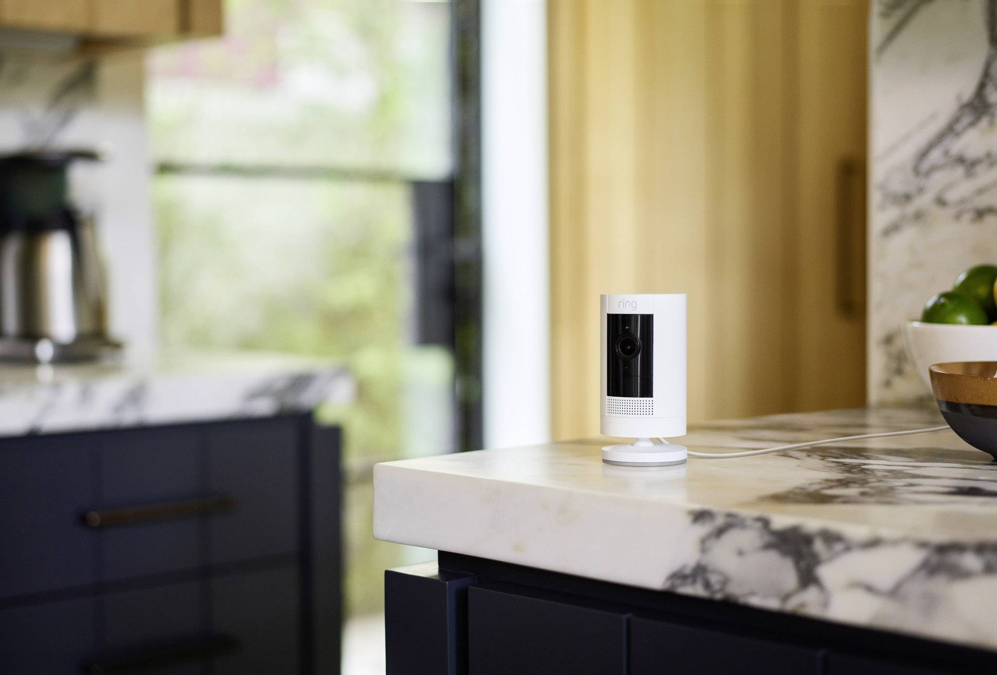Une petite caméra de surveillance blanche est posée sur un comptoir de cuisine en marbre, avec des éléments de cuisine flous en arrière-plan.