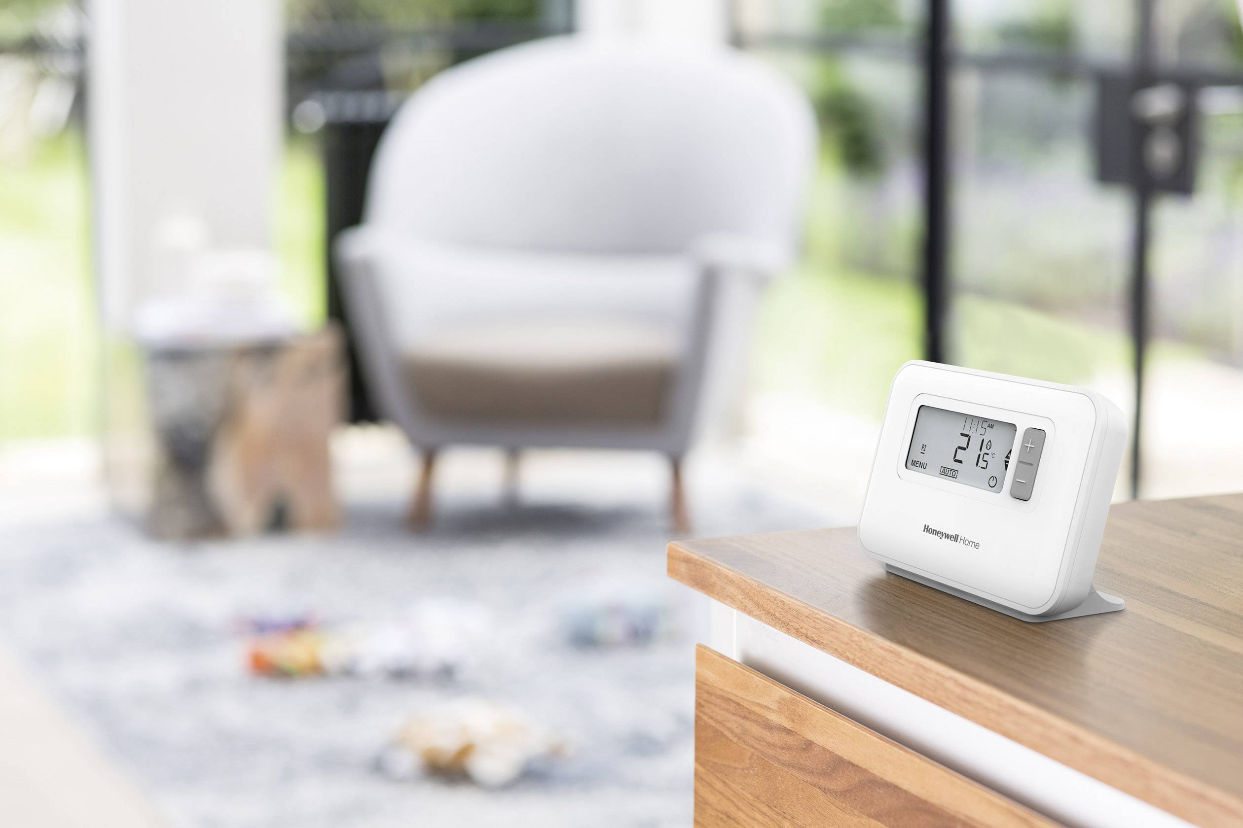 Un thermostat numérique affiche 21 degrés Celsius et est posé sur une surface en bois. Des meubles flous sont visibles en arrière-plan.