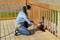 Une personne peint une terrasse en bois avec un dispositif de peinture et porte un masque de protection pour sa sécurité en extérieur.