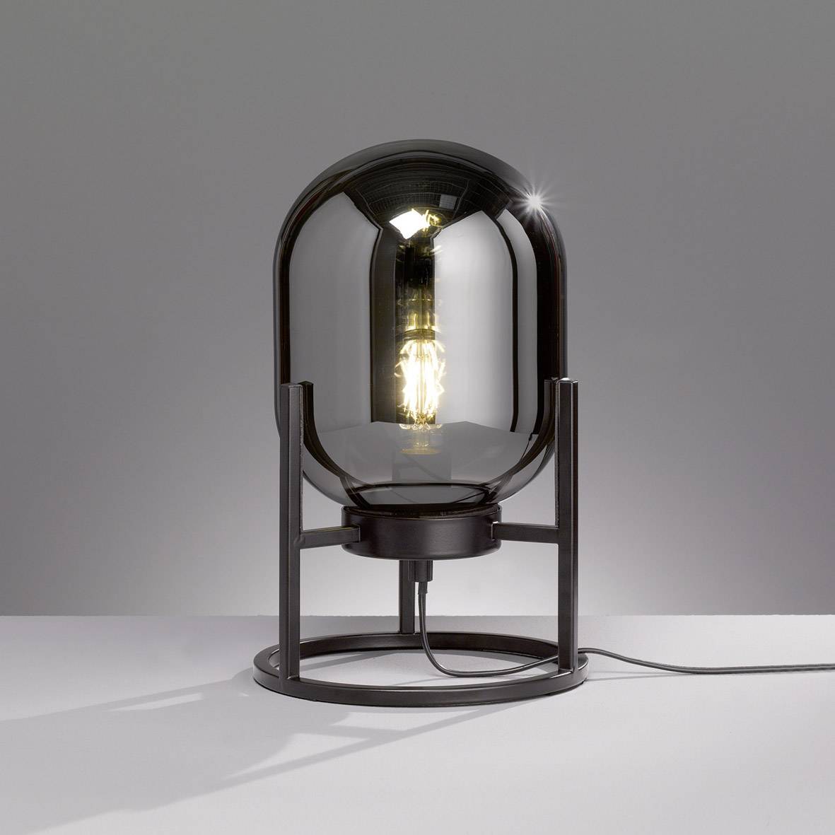 Une lampe de table moderne avec un globe en verre transparent et sphérique, dont l'ampoule est visible, est posée sur un support métallique.