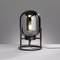 Une lampe de table moderne avec un globe en verre transparent et sphérique, dont l'ampoule est visible, est posée sur un support métallique.