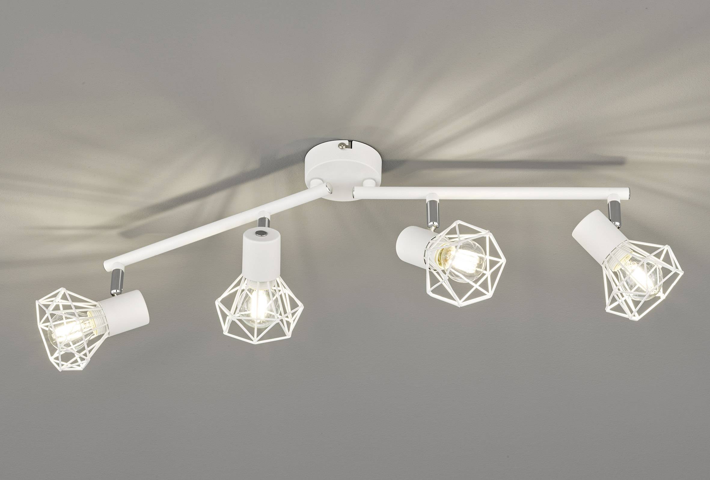 Plafonnier composé de quatre supports en métal blanc aux formes géométriques, projetant une lumière uniforme sur un plafond gris.