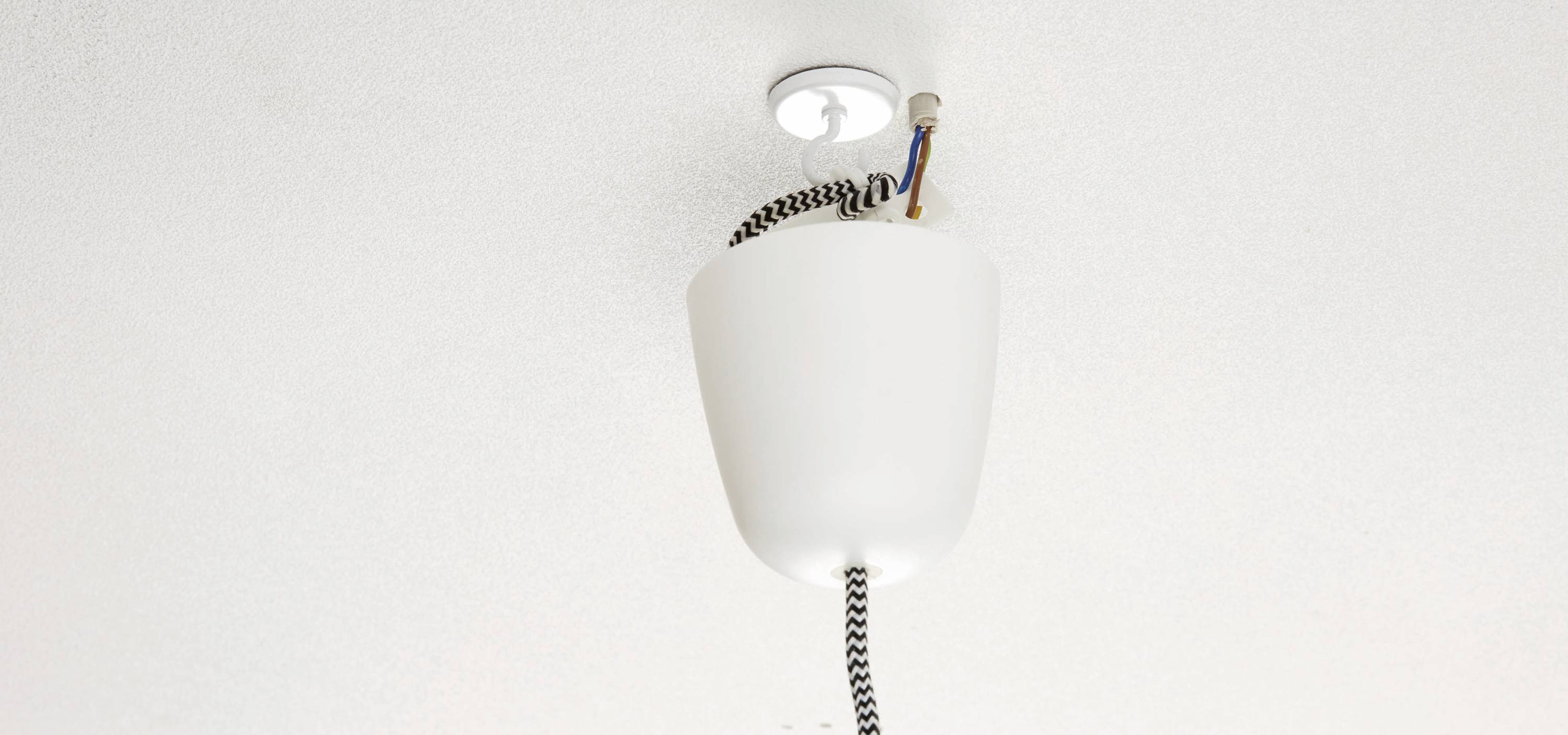 Un luminaire suspendu blanc est accroché au plafond, avec le câblage apparent. L'abat-jour est retourné et pas encore fixé.