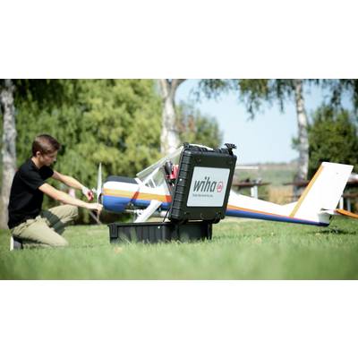 Un homme est agenouillé dans un pré et travaille sur un grand modèle d'avion, à côté de lui se trouve une mallette à outils noire de Wiha.