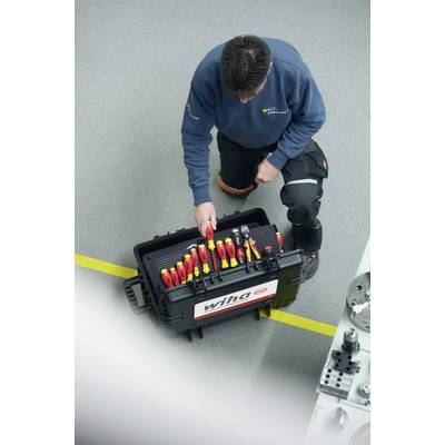 Un technicien est à genoux à côté d'une boîte à outils ouverte sur un sol gris. La boîte contient divers outils.