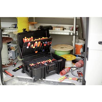 Boîte à outils ouverte dans le coffre d'un utilitaire, remplie de tournevis et de pinces. Des bobines de câbles et des outils sont visibles en arrière-plan.