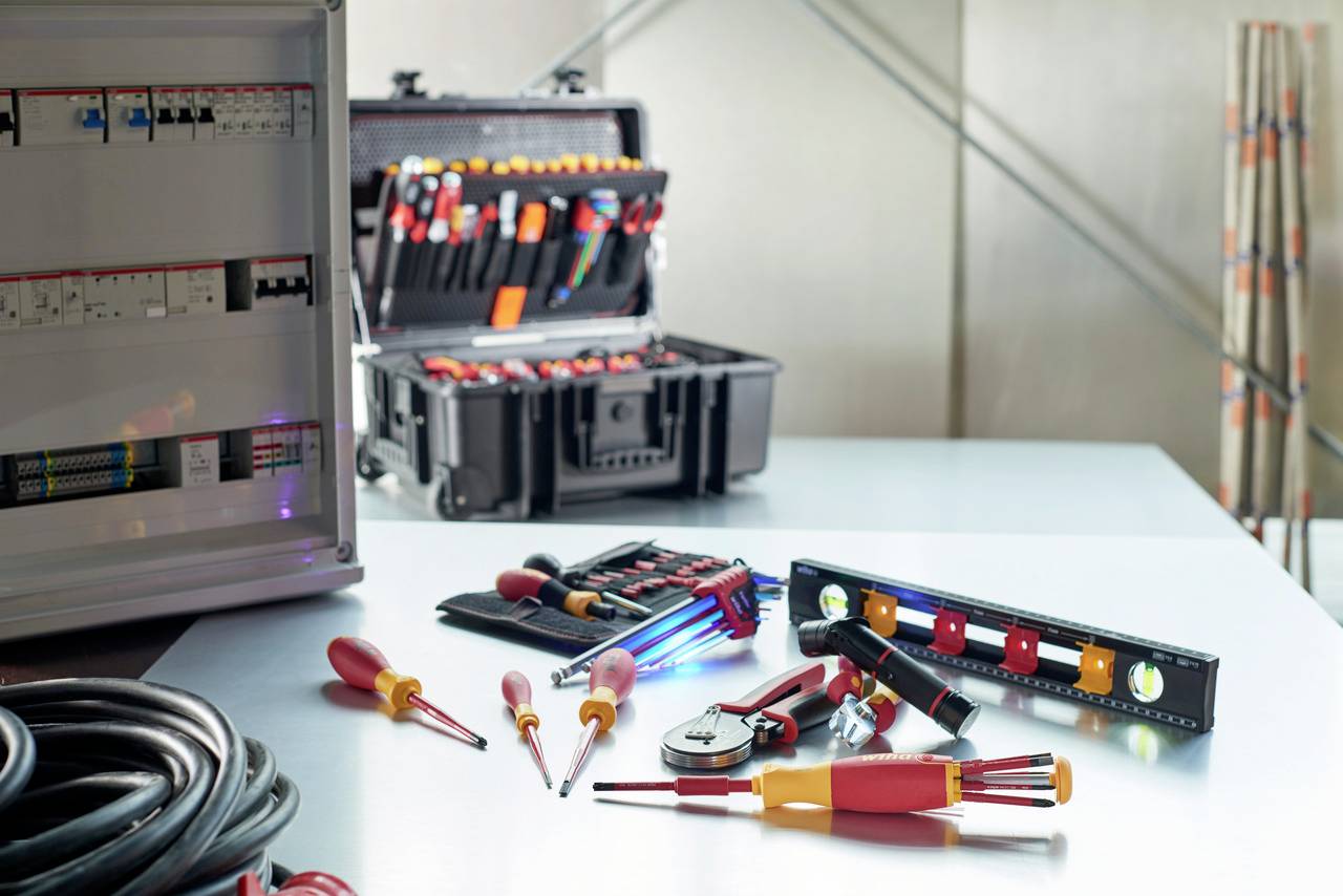 Ensemble d'outils comprenant des tournevis et des pinces sur une table, à côté d'une boîte à outils ouverte et d'un coffret électrique.