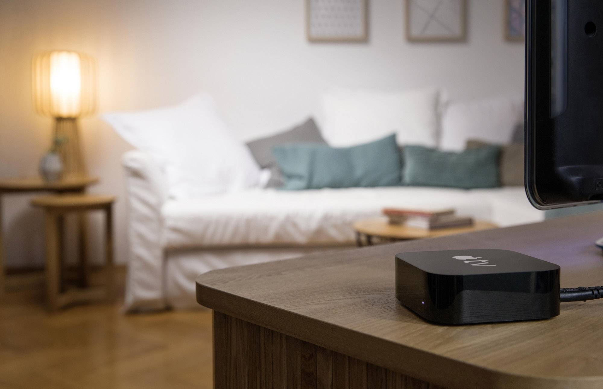 Une petite boîte TV noire est posée sur une table dans un salon confortable avec un canapé blanc et un éclairage doux.