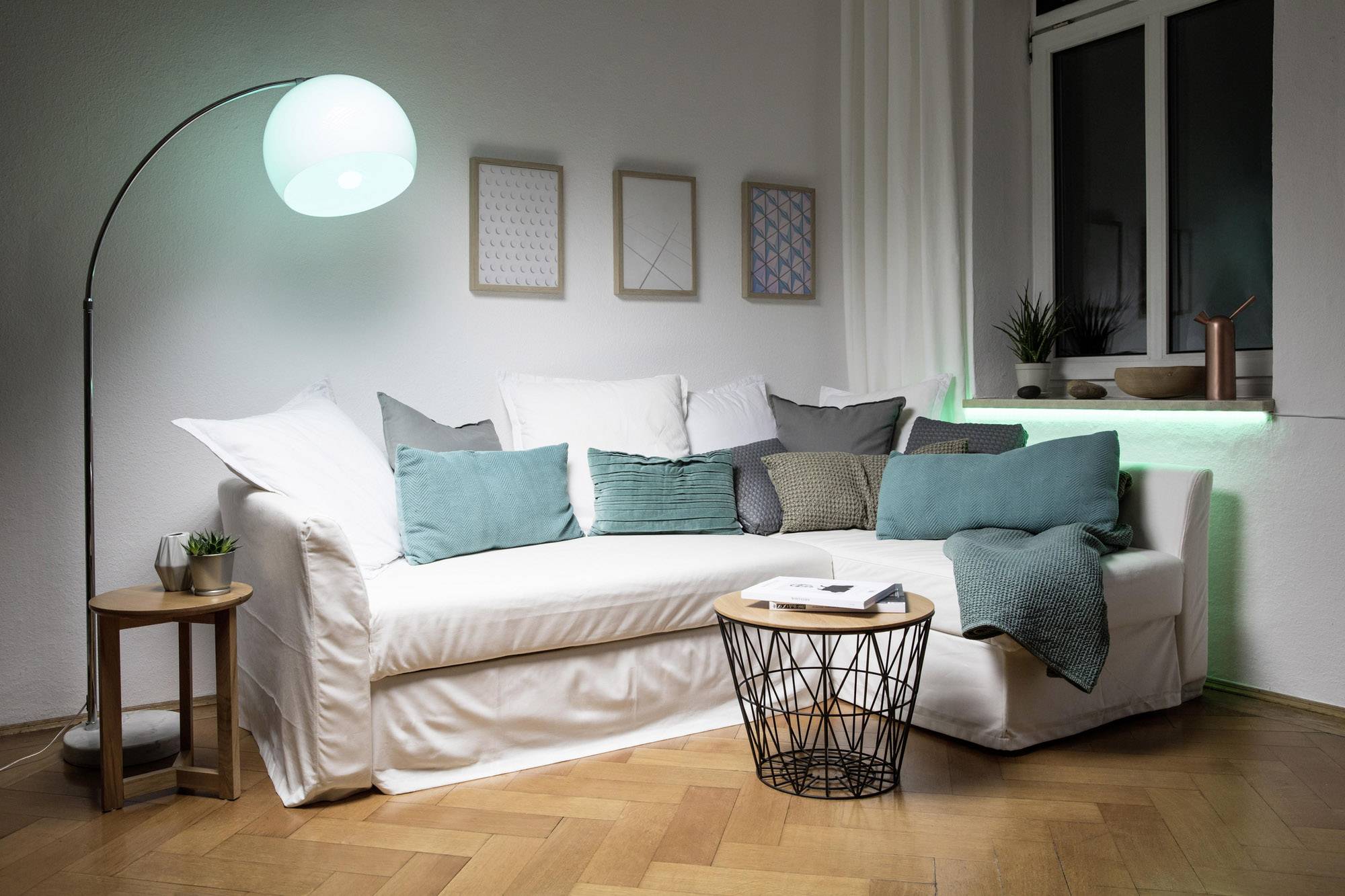 Un salon moderne avec un canapé blanc, des coussins turquoise, une table basse ronde, un lampadaire et une œuvre d'art murale.