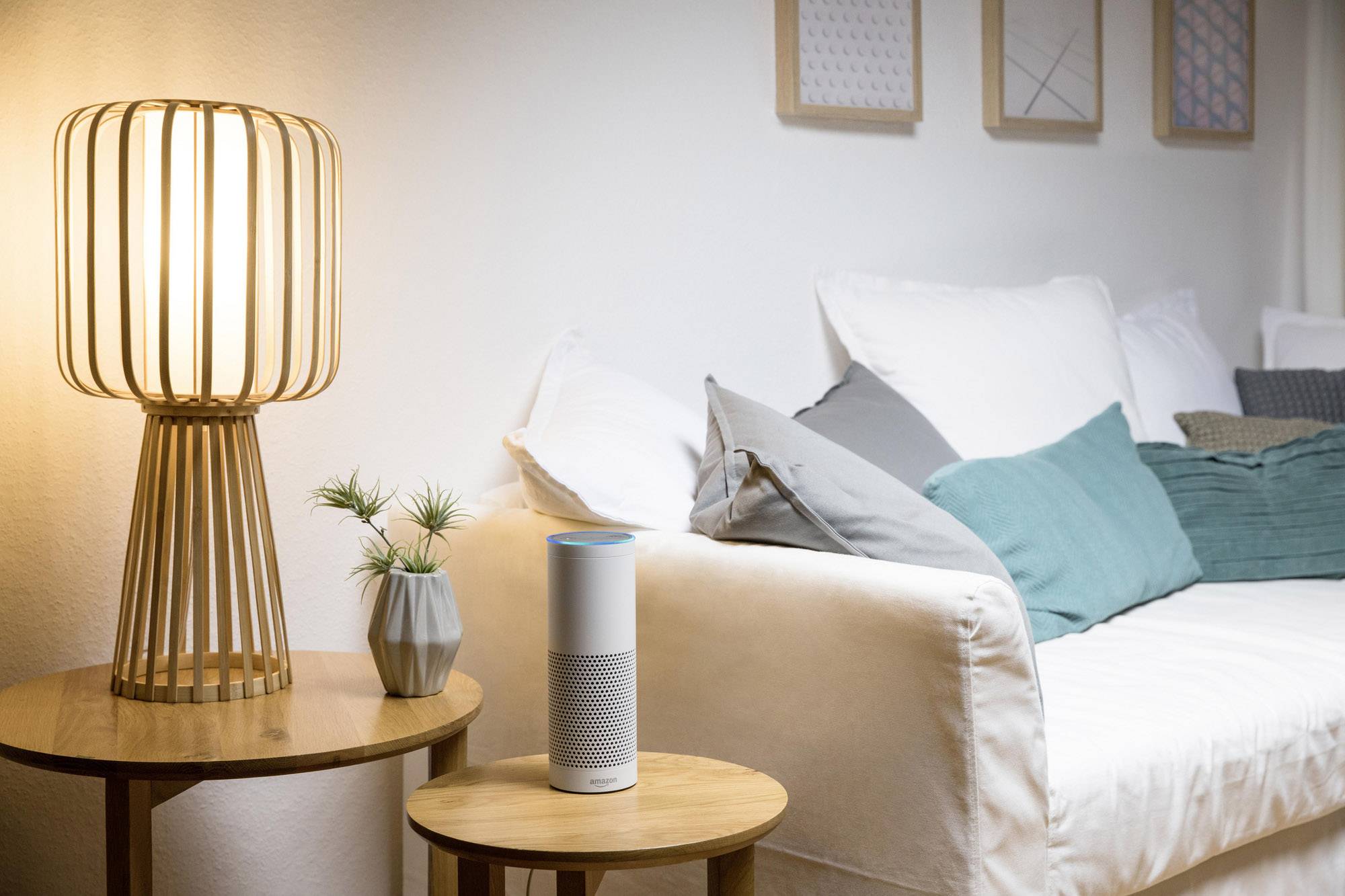 Un salon avec un canapé blanc et des coussins colorés, une lampe sur une table et un assistant vocal numérique au centre.