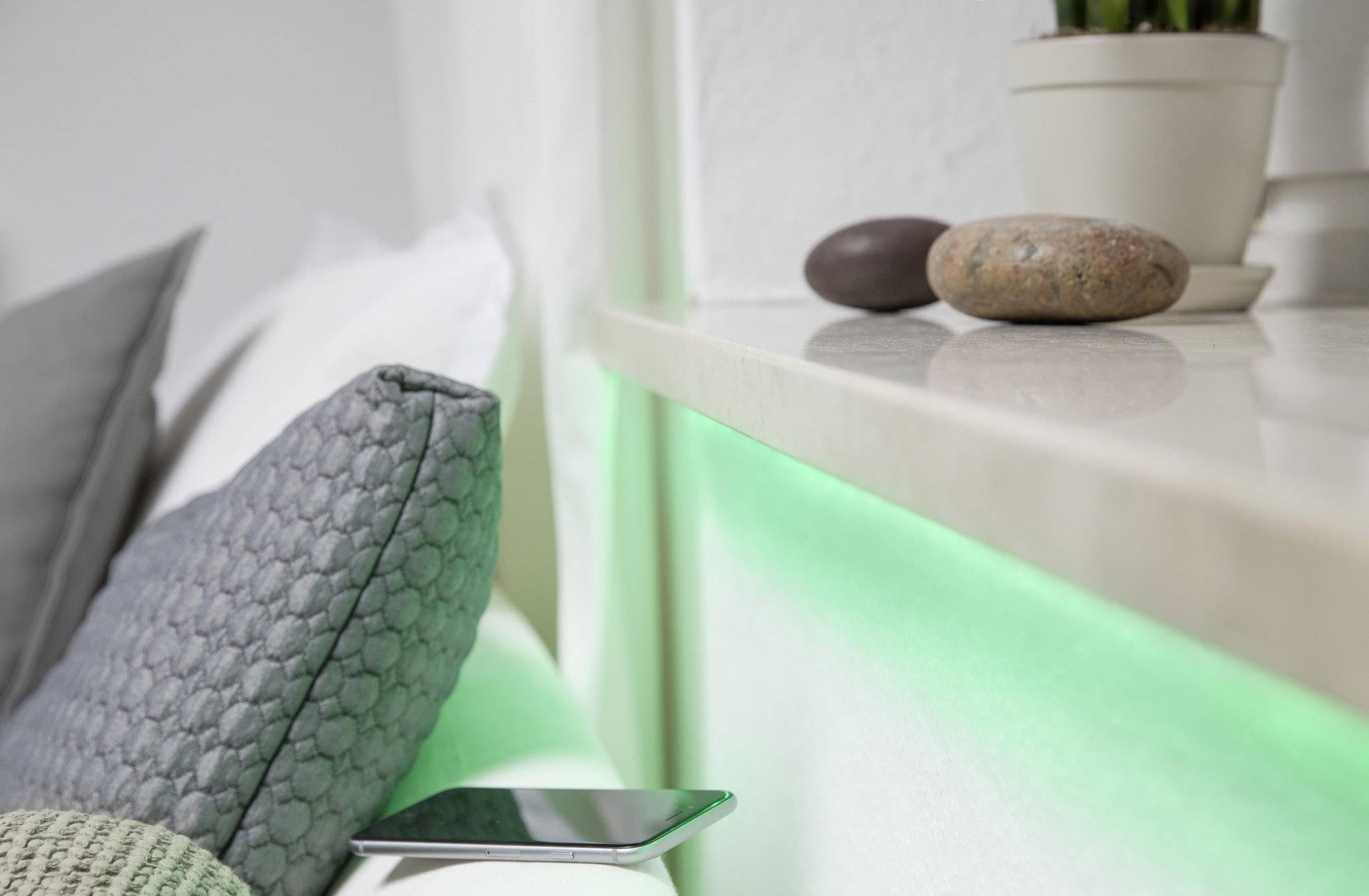 Un smartphone est posé sur une table à côté d'un coussin gris. En arrière-plan, on aperçoit des plantes d'intérieur et des pierres décoratives.