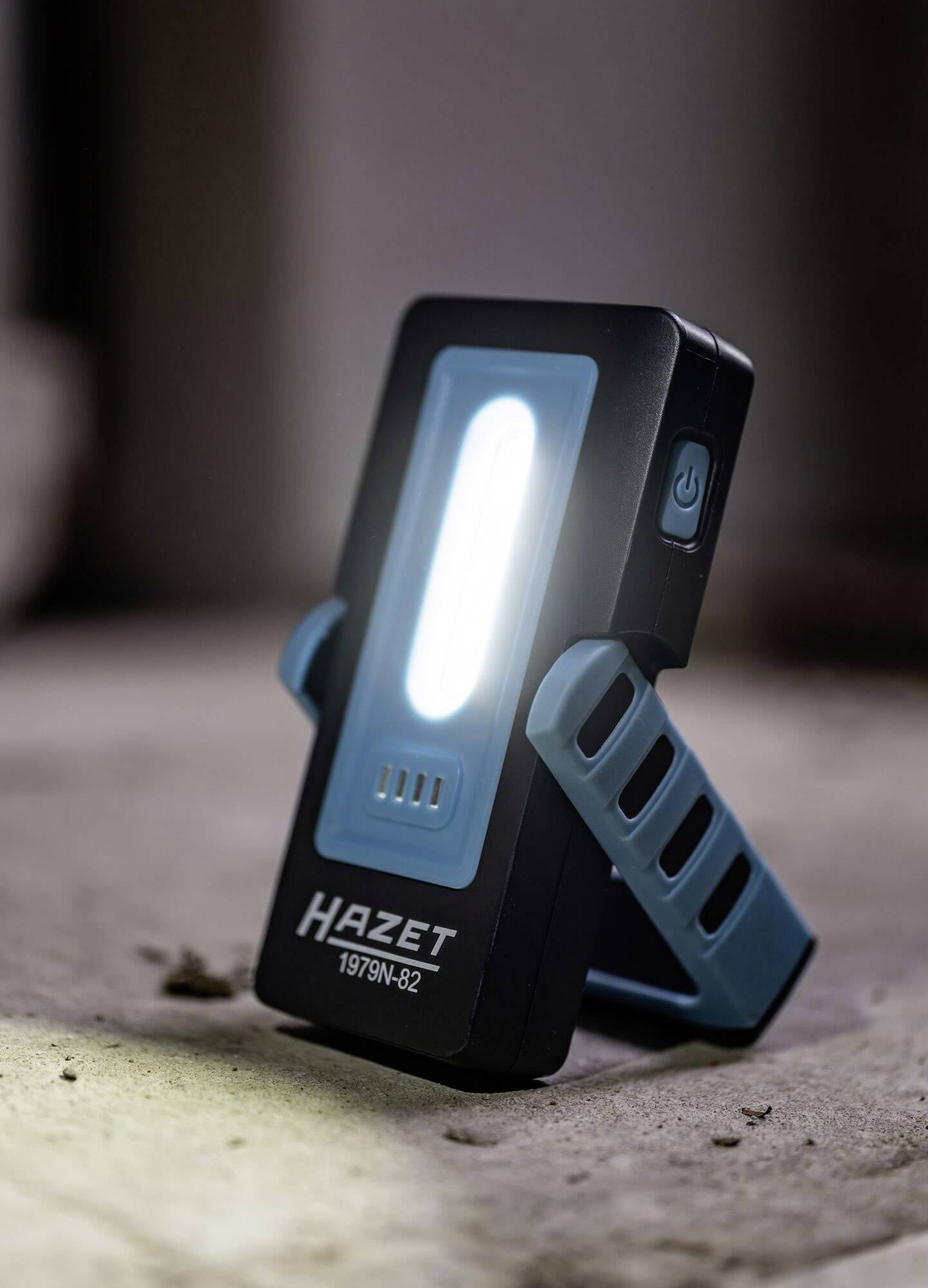 Lampe LED portable Hazet éclairant une pièce sombre. La lampe est posée sur un support pliable et diffuse une lumière vive.