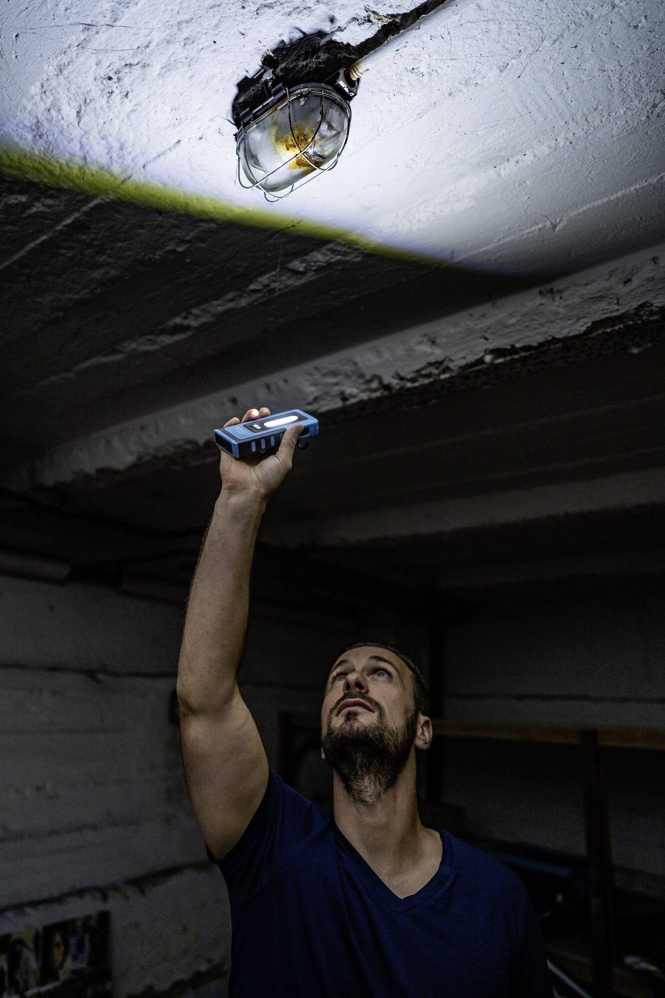 Un homme dans une pièce sombre tient un appareil de mesure en l'air pour mesurer la hauteur jusqu'au plafond, tout en regardant vers le haut.