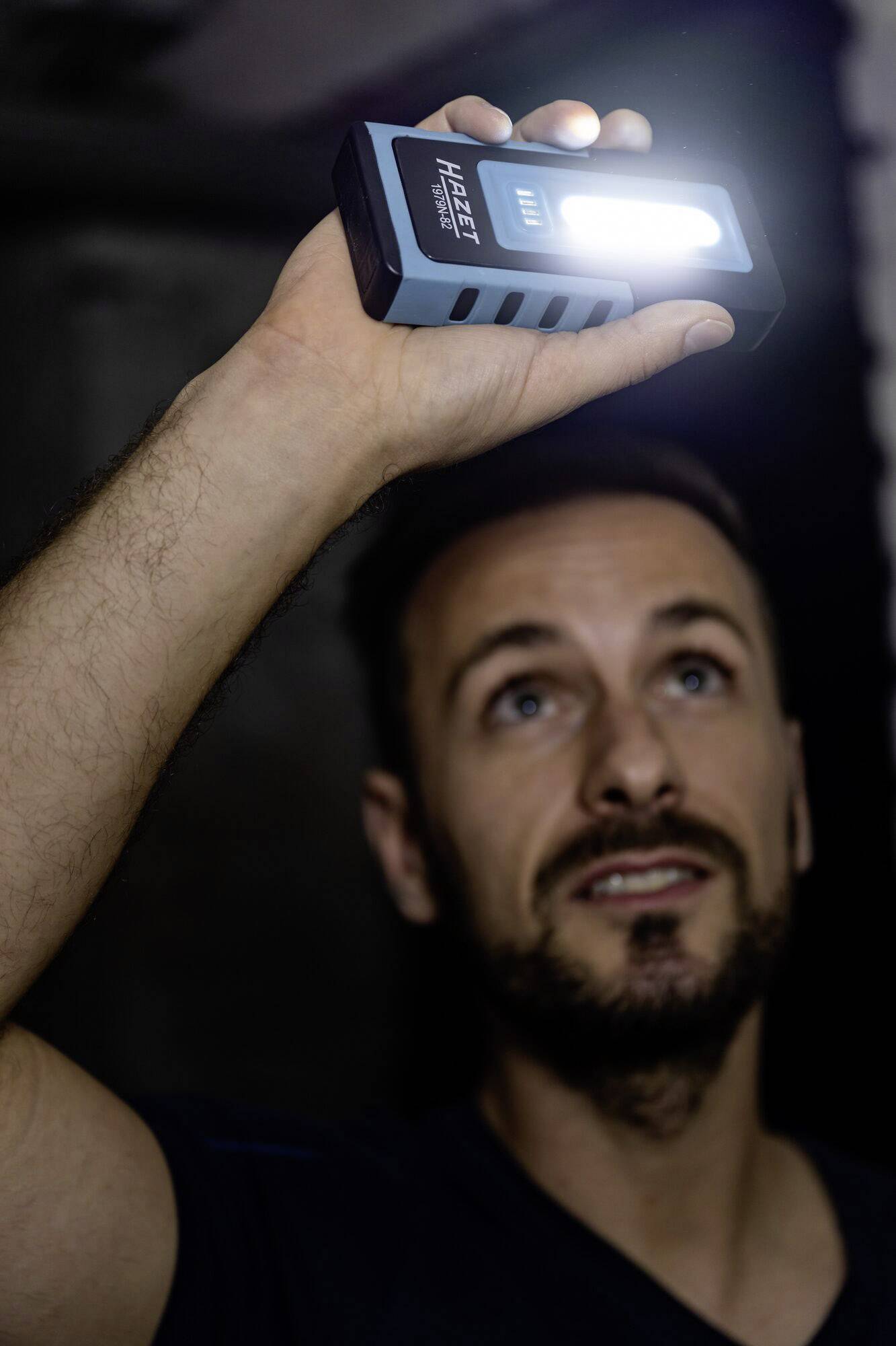 Un homme tient une lampe de poche allumée vers le haut, illuminant une pièce sombre.