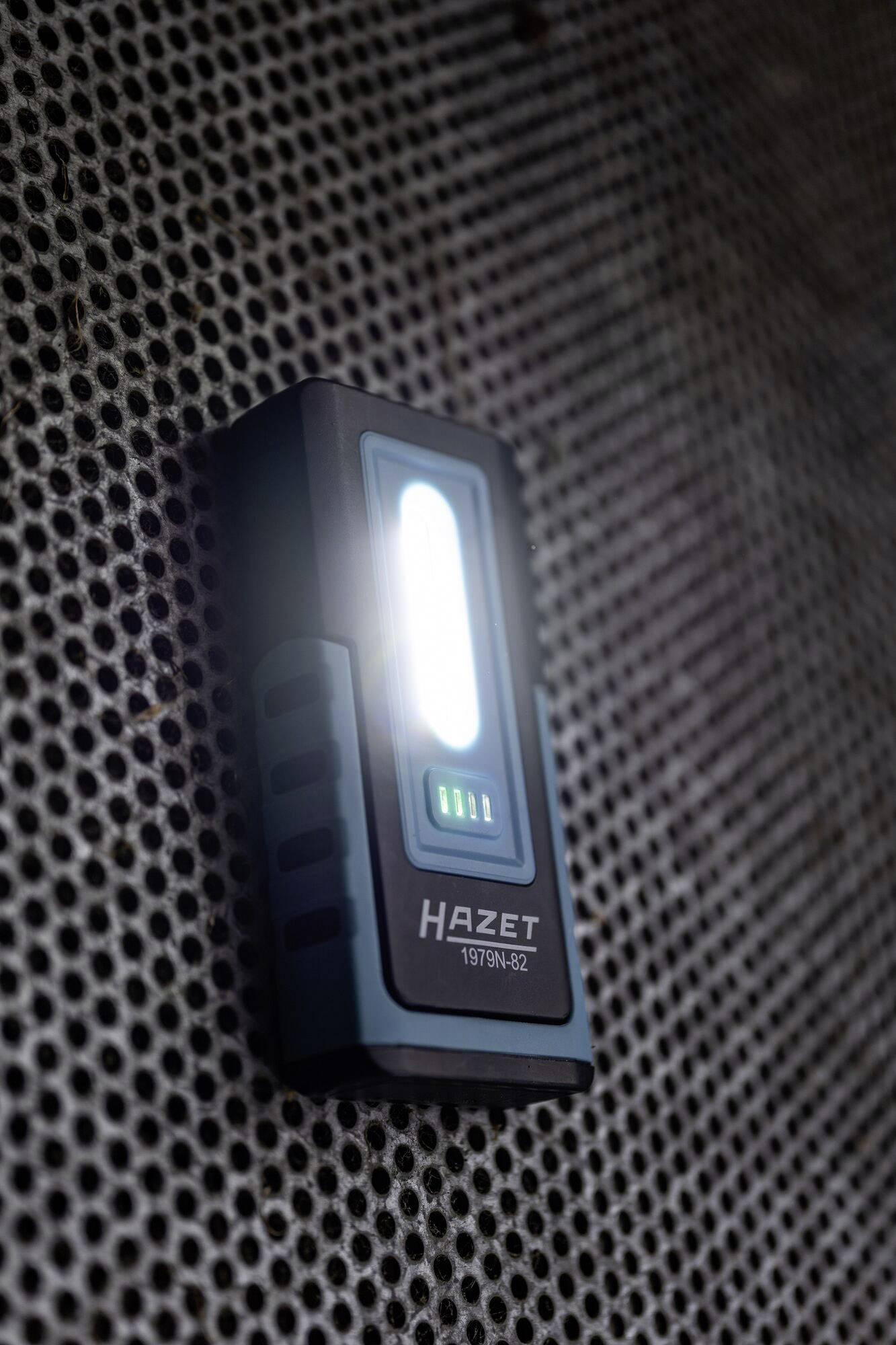 Une lampe LED portable rectangulaire de Hazet s'illumine brillamment sur un fond sombre perforé.