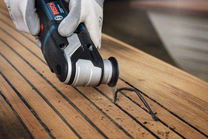 Un outil électrique retire l'ancien mastic des lattes de bois. Une personne portant des gants effectue le travail avec soin.