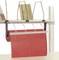 Une étagère avec des garnitures métalliques, sur laquelle sont posés des objets plats. En dessous, un rouleau de papier rouge est suspendu à un support.