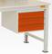 Une partie d'une table de travail blanche avec trois tiroirs oranges. Les pieds de la table sont métalliques.