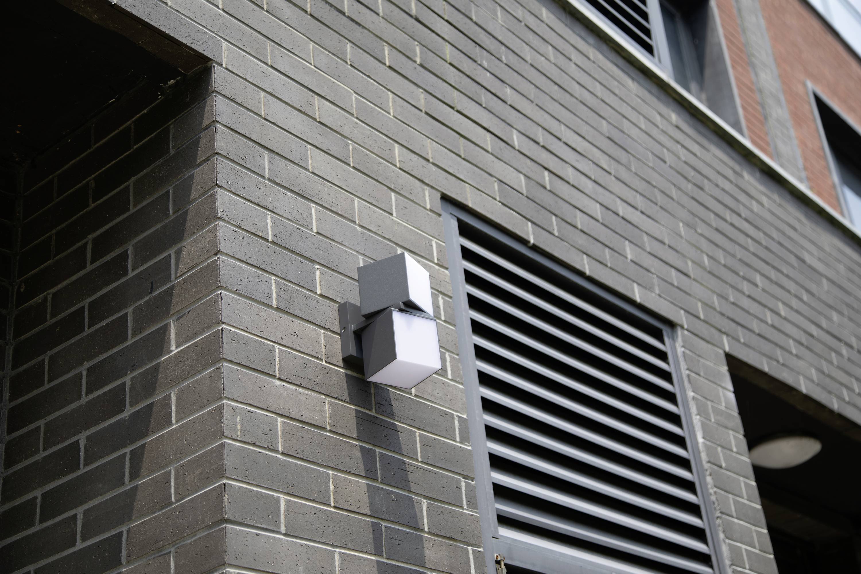 Applique murale extérieure sur un mur de briques gris d'un bâtiment, près d'une fenêtre ventilée ; architecture moderne.