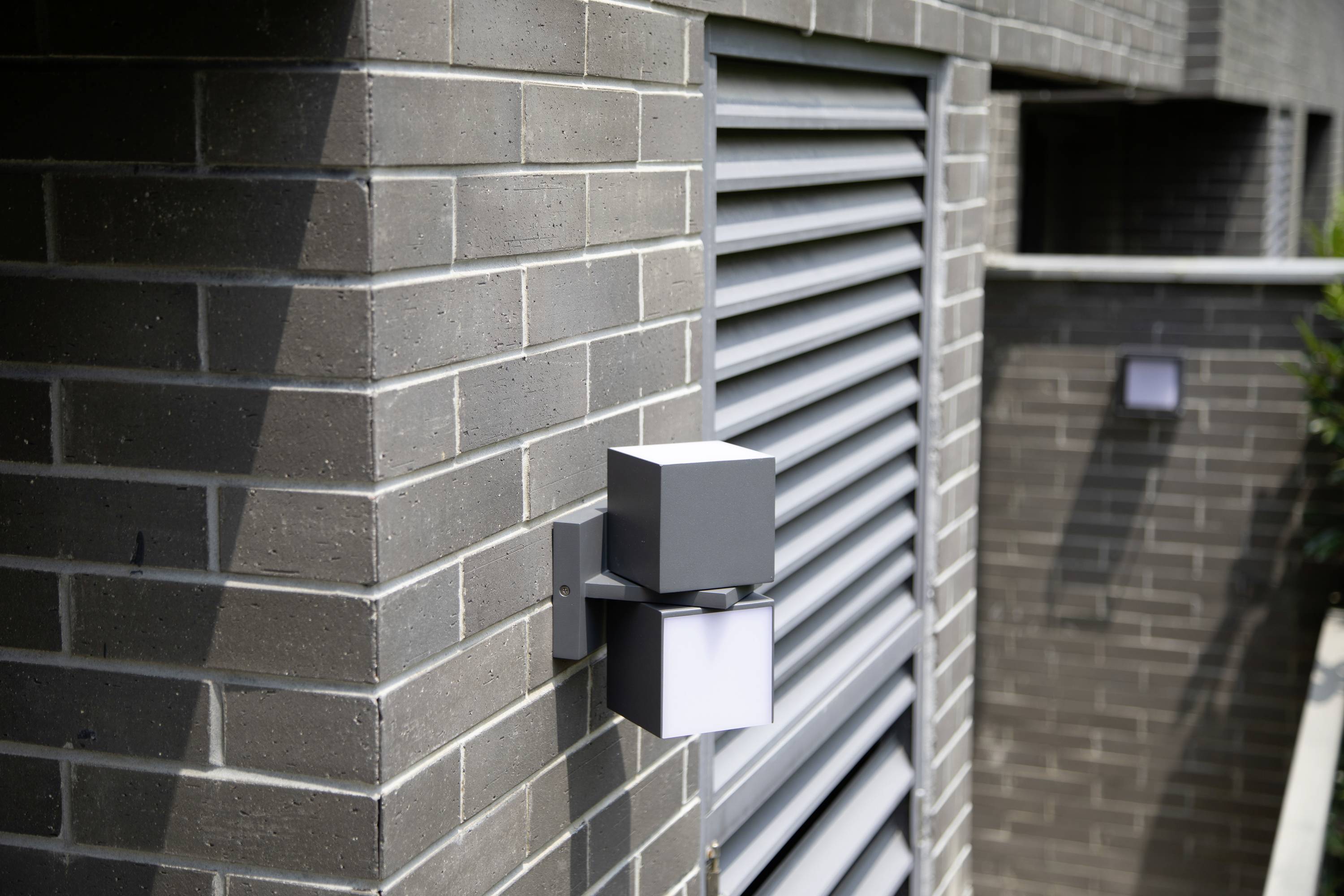 Applique murale moderne en briques, design géométrique, à côté d'une fenêtre à lamelles. Luminaire assorti en arrière-plan.
