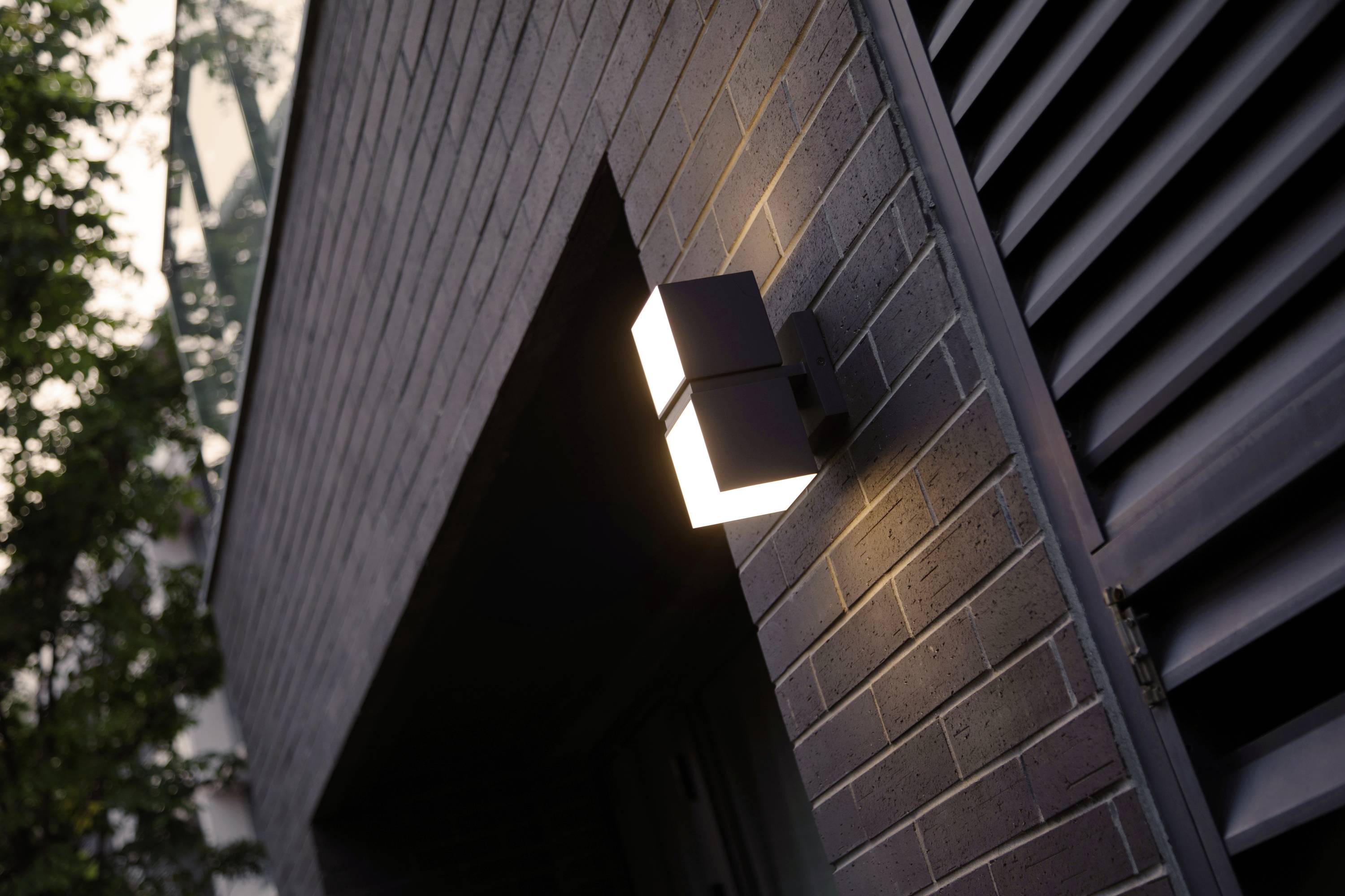 Éclairage extérieur sur le mur de briques d'un bâtiment au crépuscule, illuminant la zone d'entrée.