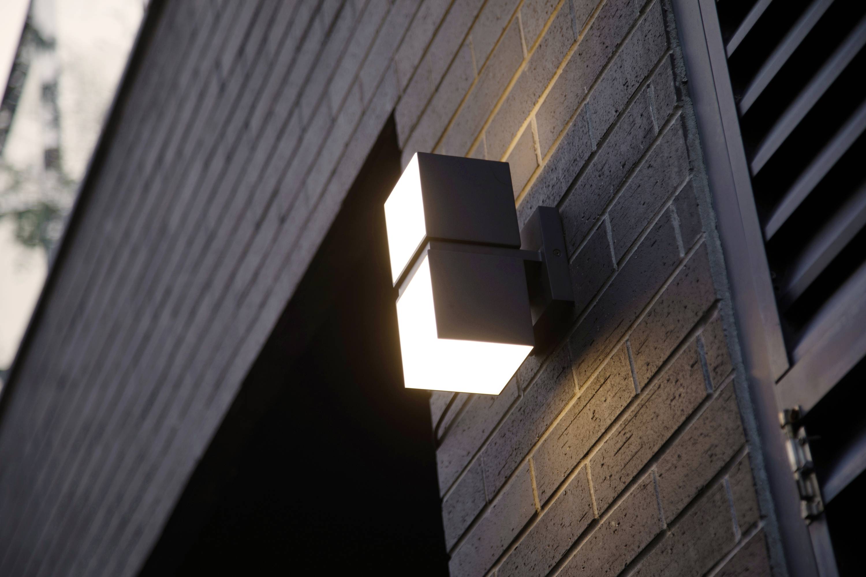 Un luminaire mural moderne éclaire un mur de briques, illuminant l'entrée ou le chemin.