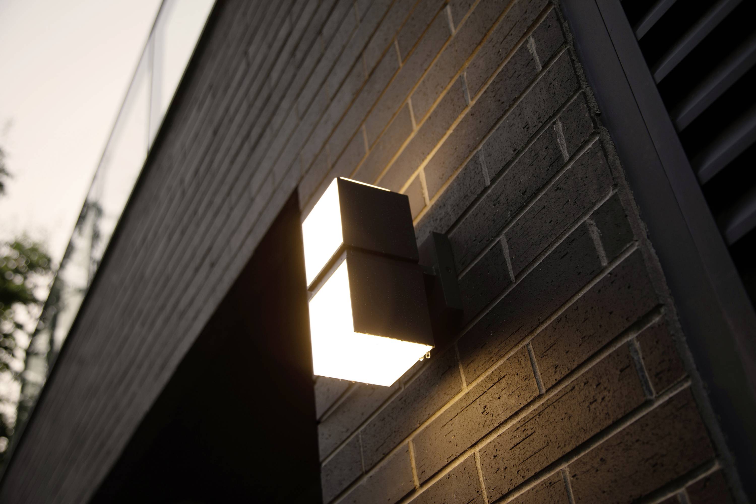 Applique murale sur un mur de briques, diffusant une lumière chaleureuse. Idéale pour les espaces extérieurs modernes ou comme accent architectural.