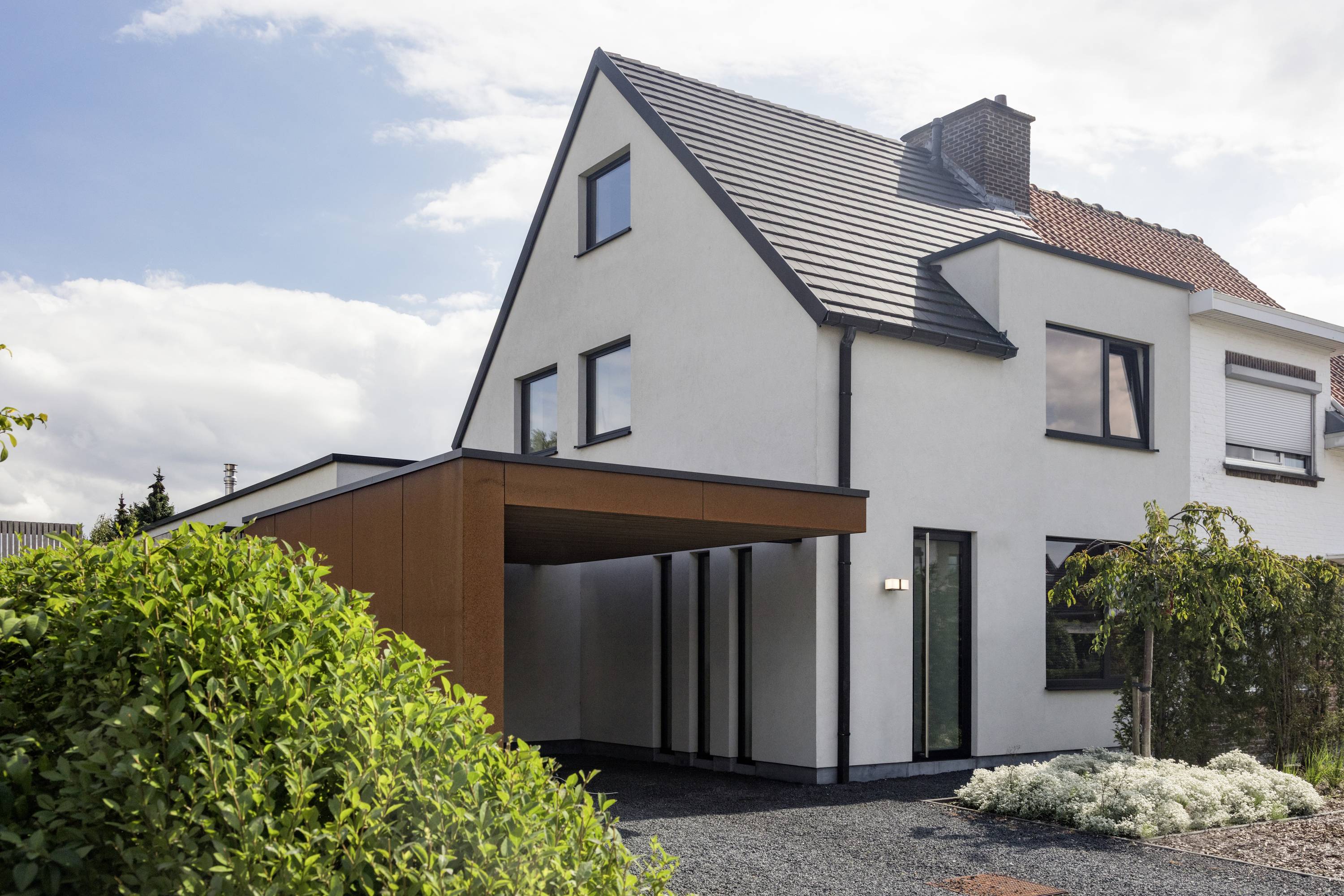 Maison individuelle moderne avec toit à deux pans et carport attenant, entourée d'un jardin bien entretenu. Façade claire, lignes épurées.