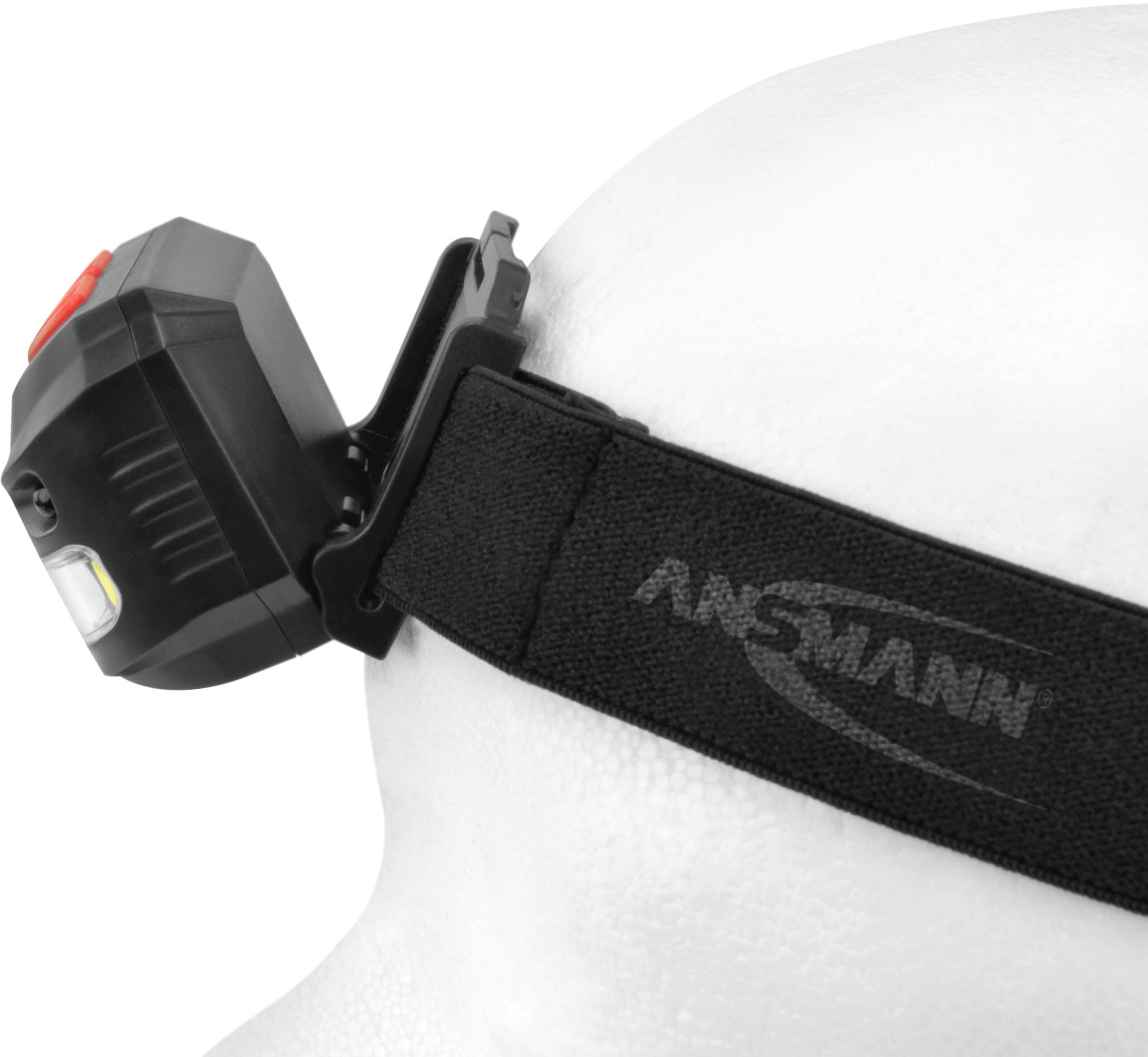 Lampe frontale sur un modèle de tête, bandeau noir avec le logo 'ANSMANN', lampe rectangulaire avec un bouton rouge et un éclairage LED.