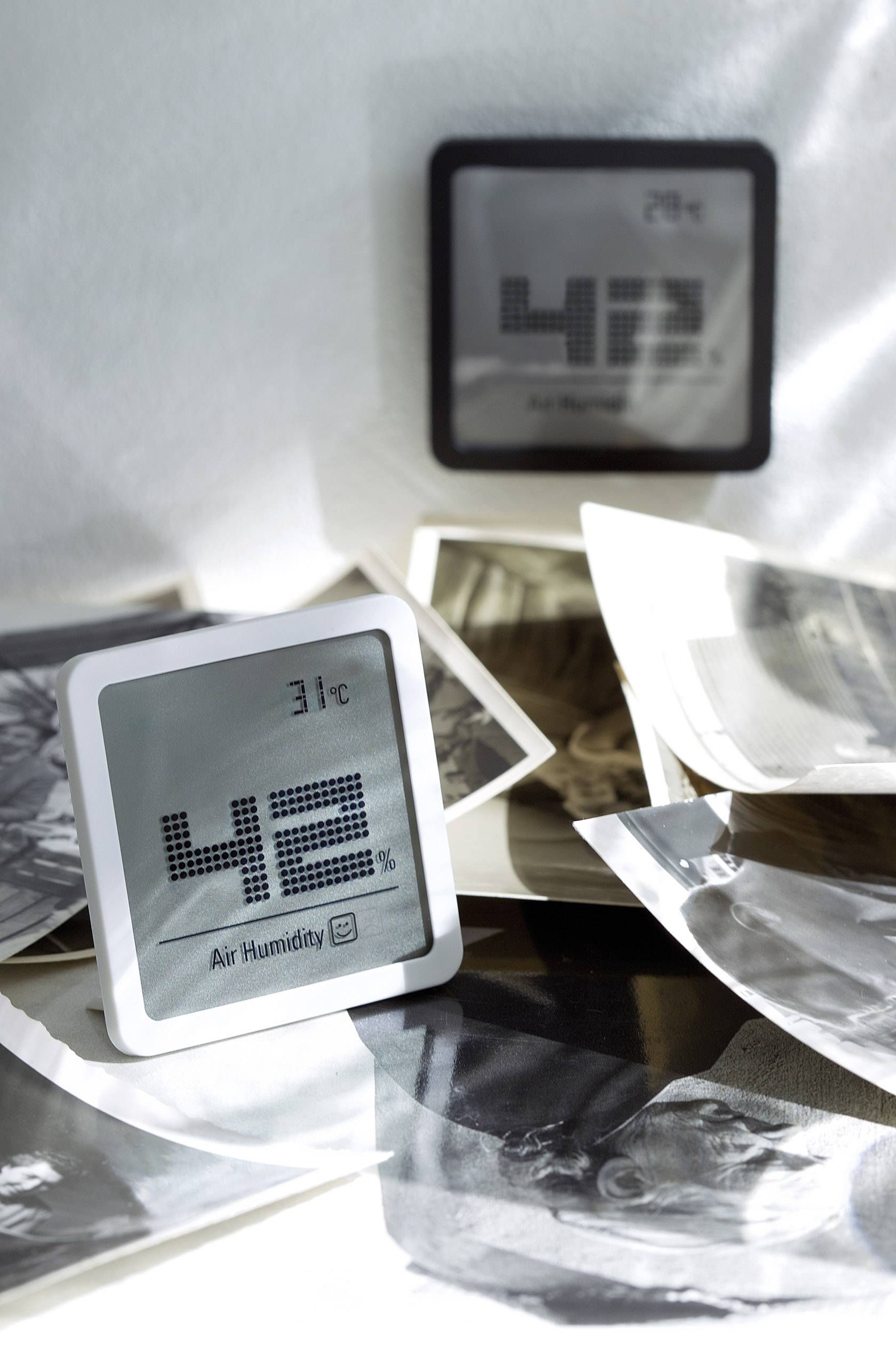 Un hygromètre numérique affiche 31°C et 42% d'humidité relative, entouré de photographies en noir et blanc sur une table.