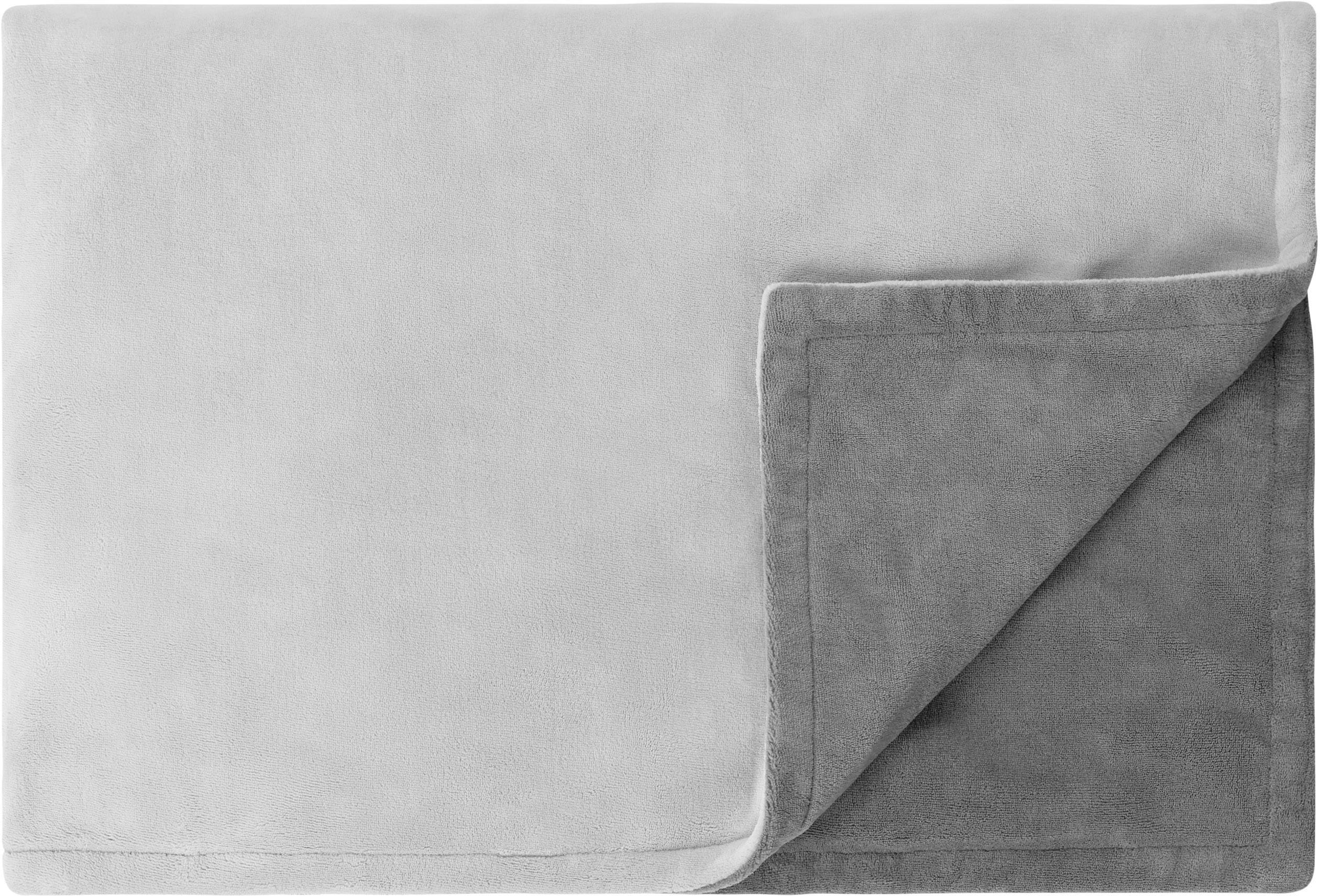Couverture grise à double épaisseur, repliée et montrant des côtés gris plus clairs et plus foncés. Matériau doux et duveteux.