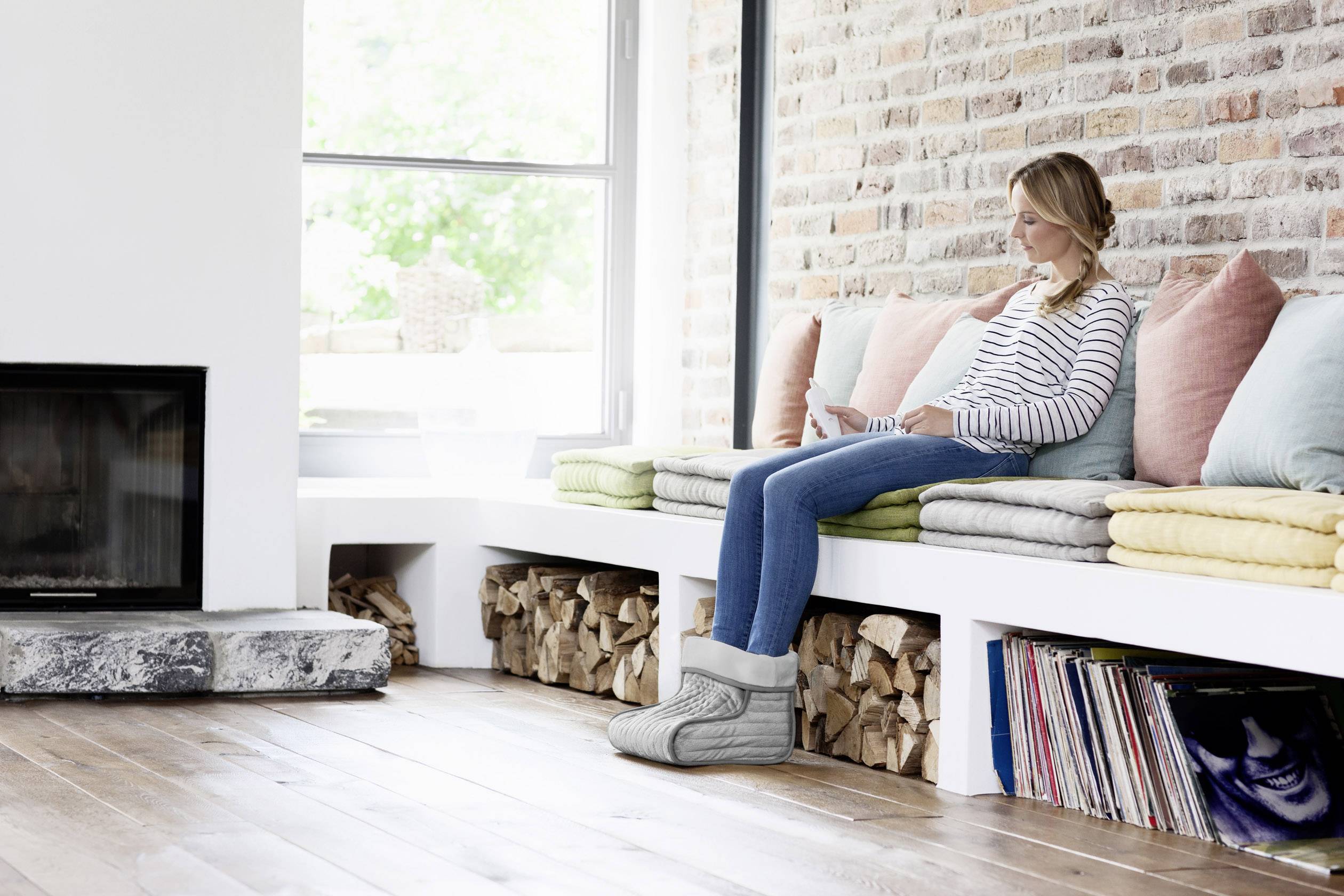 Une femme est assise sur le rebord de la fenêtre dans un salon douillet, lit un livre et porte des pantoufles chaudes.