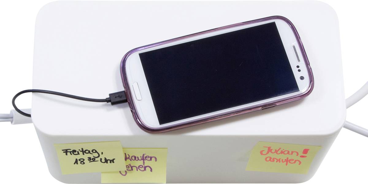 Un smartphone charge sur une boîte blanche avec deux notes autocollantes : « Acheter vendredi à 18h » et « Appeler Julian ».
