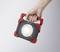 Une main tient une lampe de travail LED portable rectangulaire au boîtier rouge et noir.