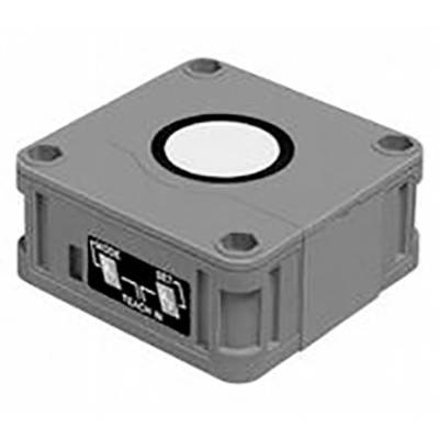 L'image montre un capteur de boîtier rectangulaire gris avec quatre trous de montage aux coins et un cercle blanc central en haut.