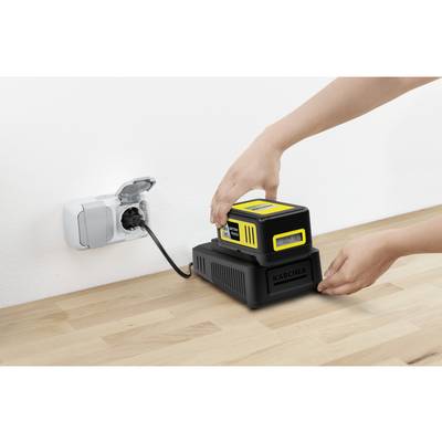 Une personne charge une batterie jaune sur une station de charge noire qui est branchée à une prise électrique.