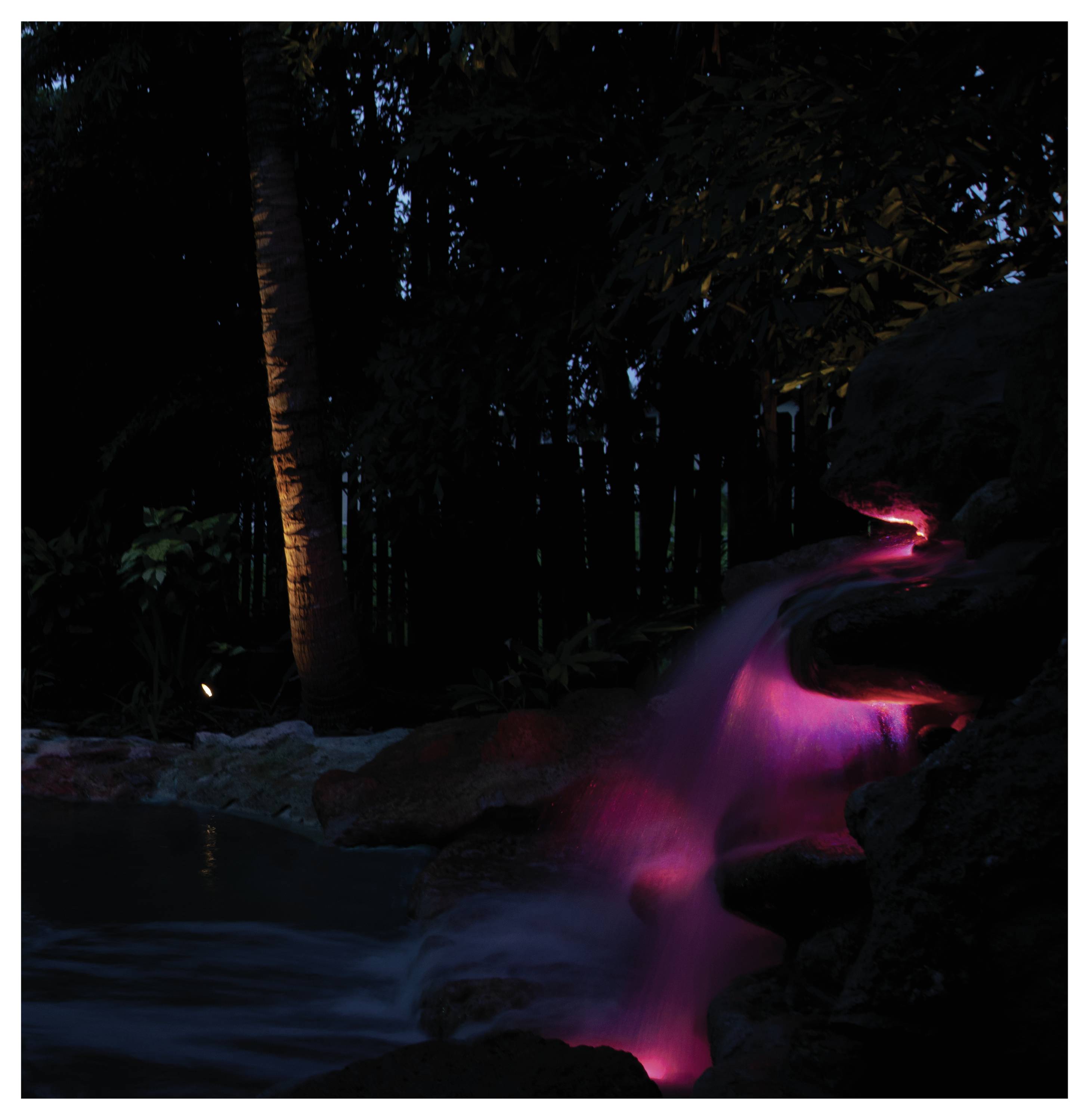 Cascade illuminée par des lumières roses dans un décor forestier sombre, créant une atmosphère sereine et mystique.