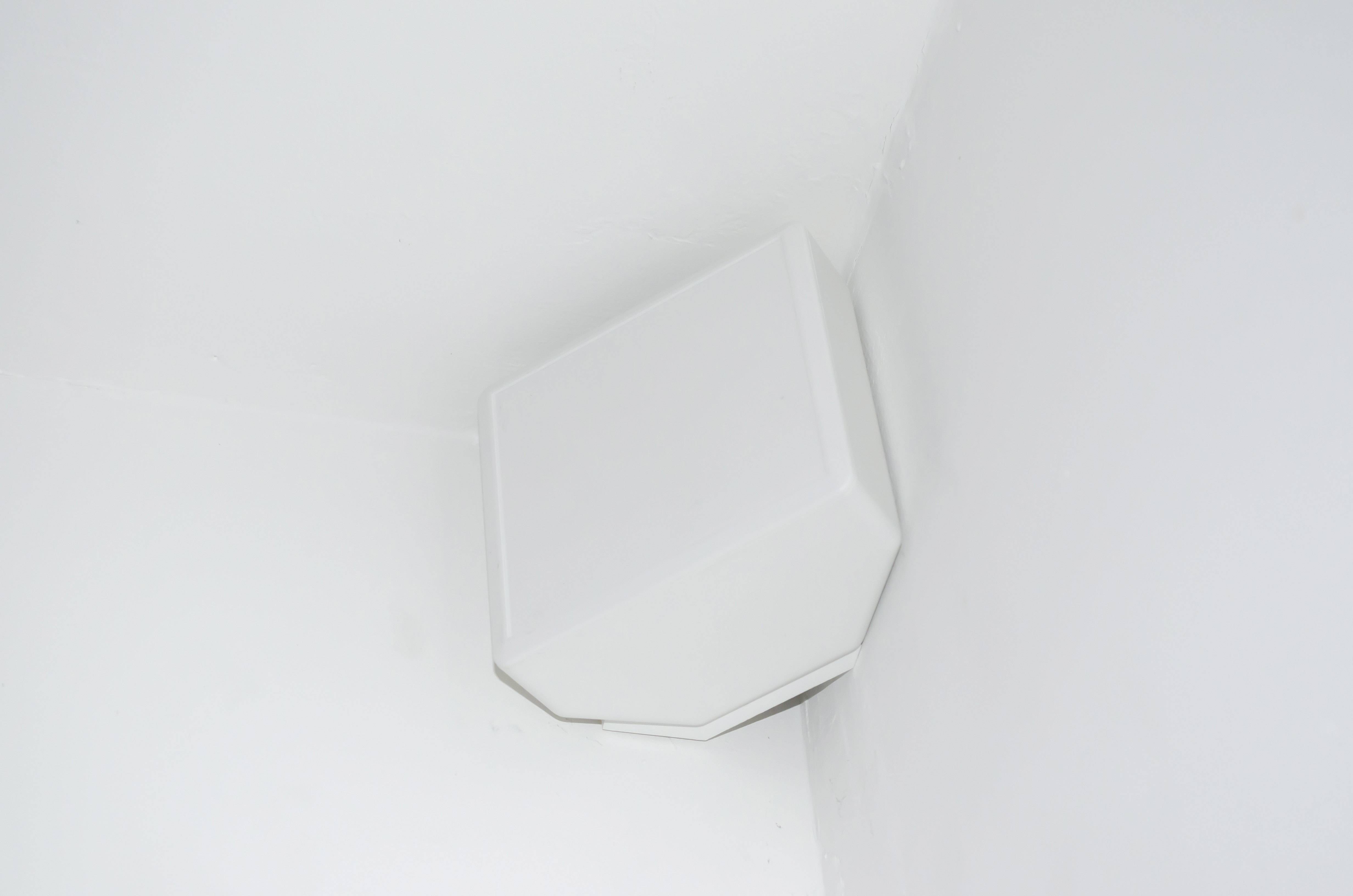 Un haut-parleur blanc est monté dans un coin de la pièce, sur le mur.