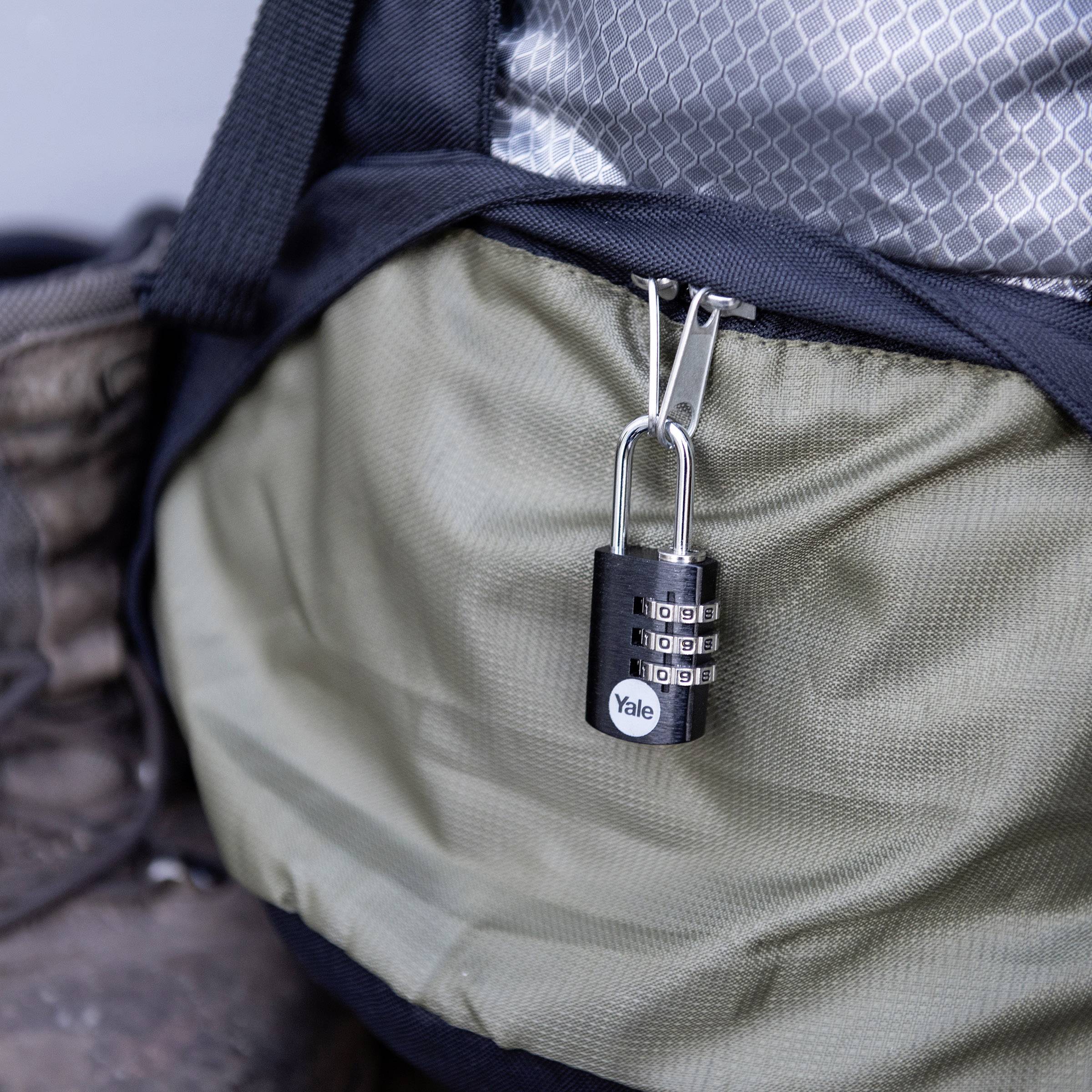 Un cadenas à code est suspendu à un sac à dos vert olive. À côté se trouve une botte. Le cadenas sert à sécuriser le sac à dos.
