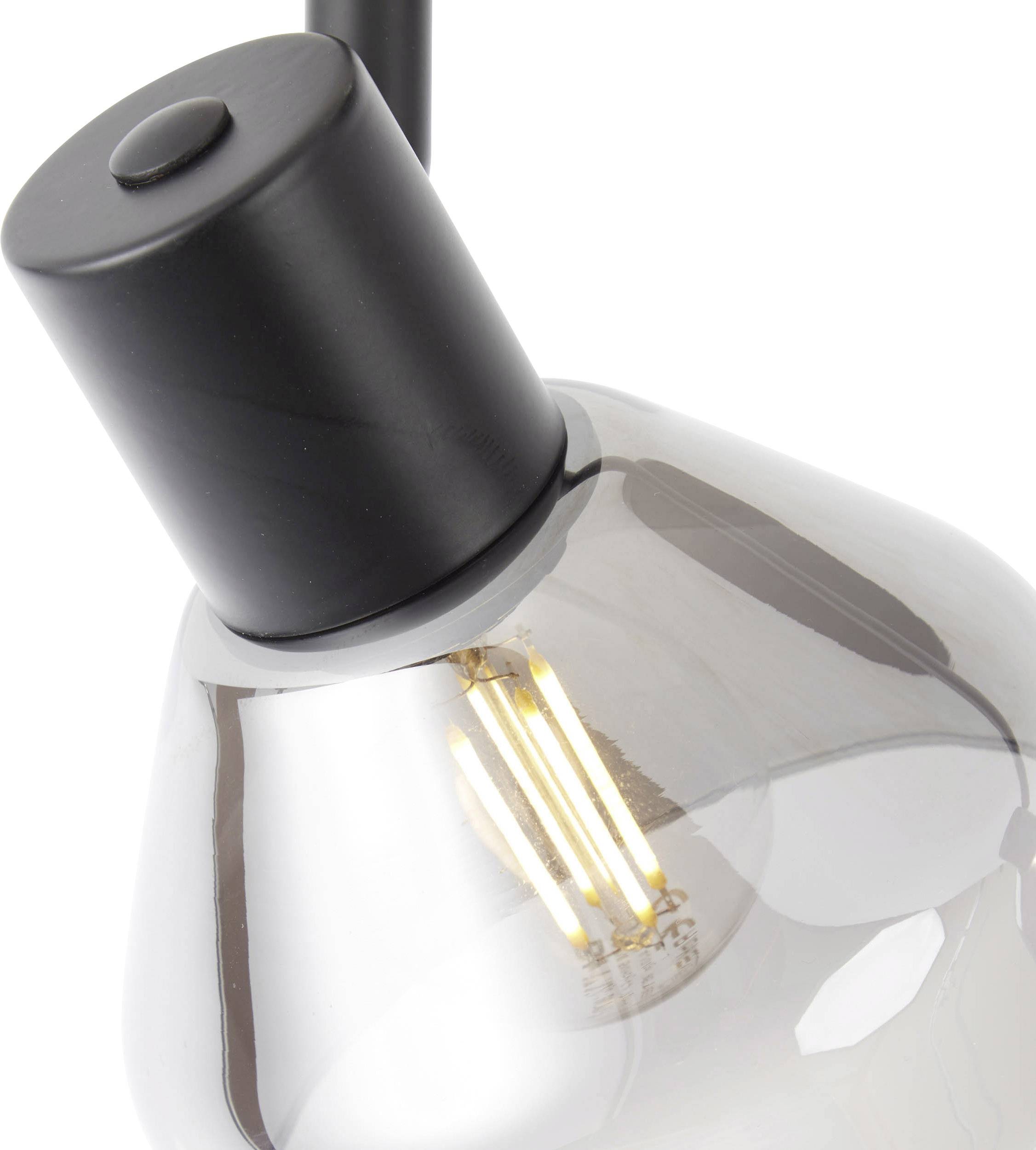 Gros plan d'une lampe moderne avec un socle noir et un abat-jour en verre gris fumé, révélant une ampoule à lueur chaleureuse.