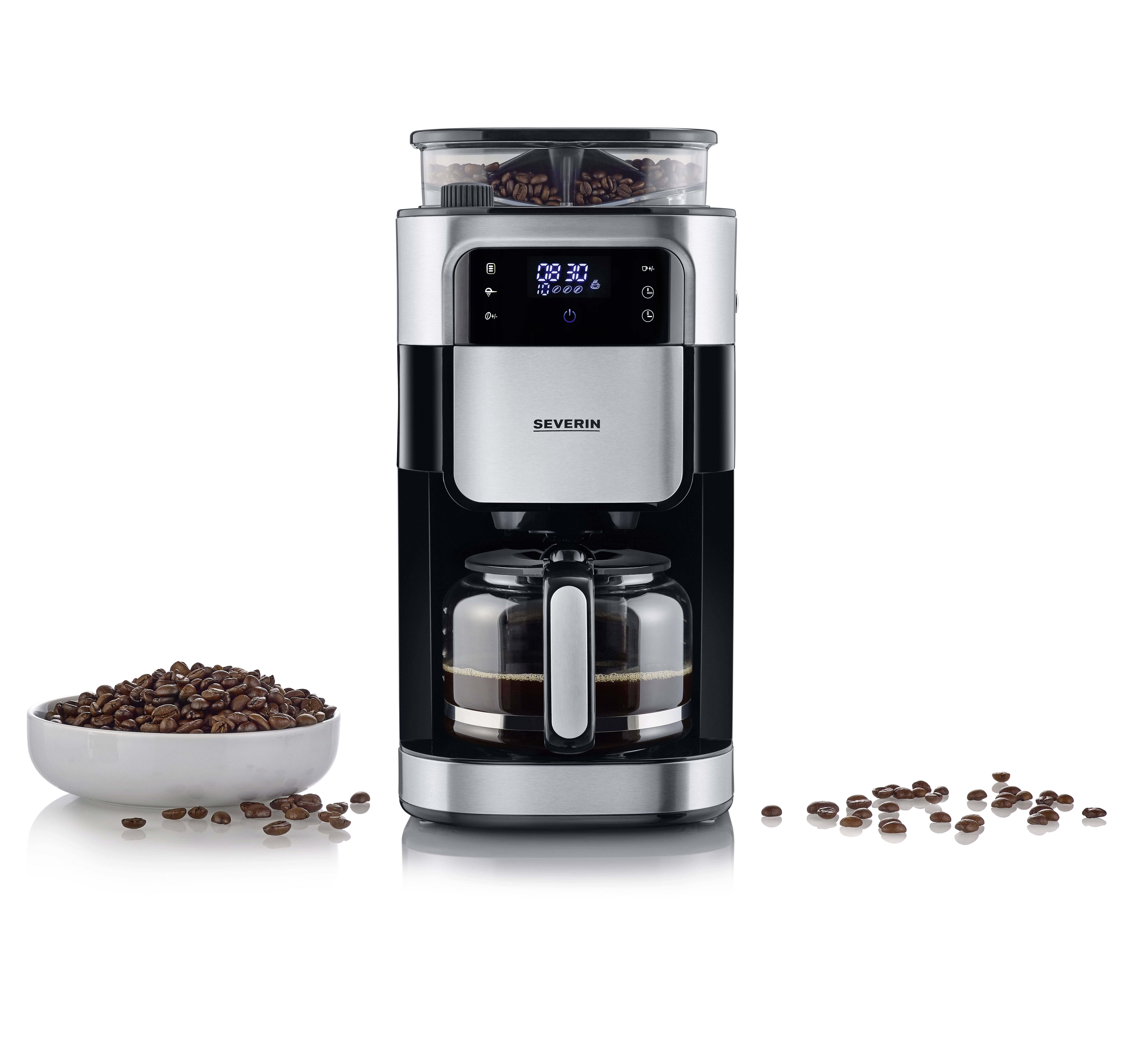 Une machine à café argentée avec un affichage numérique et une carafe en verre, disposée à côté d'un bol rempli de grains de café.